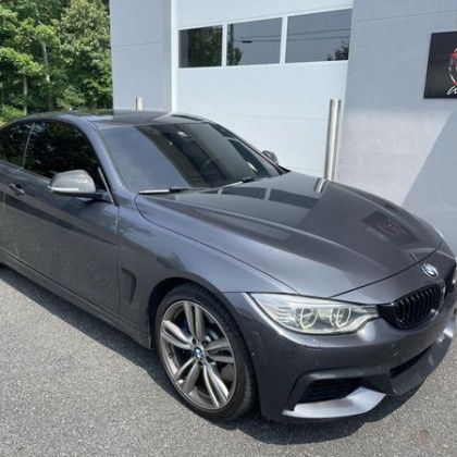 A gray bmw 4 series is parked in front of a white garage door.