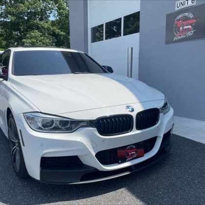 A white bmw 3 series is parked in front of a building.