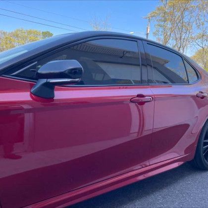 A red car is parked in a driveway on a sunny day.