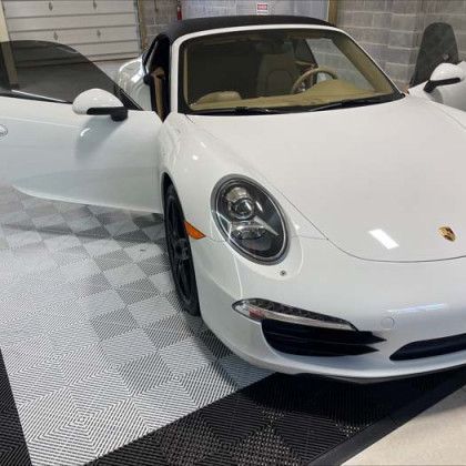 A white porsche 911 carrera is parked in a garage with its doors open.