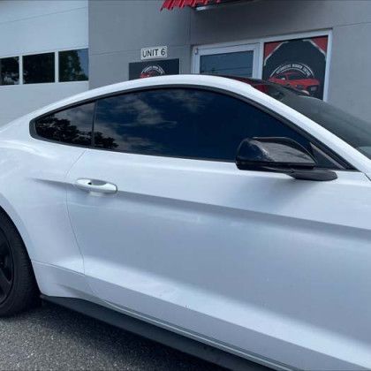 A white mustang is parked in front of a garage door.