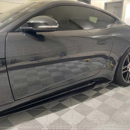 A black mustang is parked in a garage on a checkered floor.