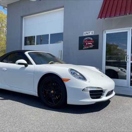 A white porsche 911 convertible is parked in front of a garage door.