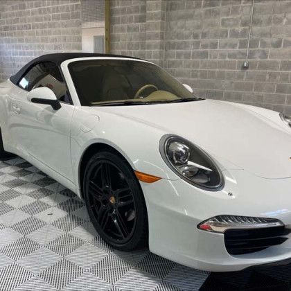 A white porsche 911 convertible is parked in a garage.