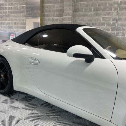 A white porsche 911 convertible with a black top is parked in a garage.