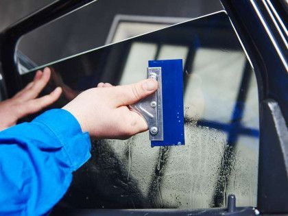 A person is applying tinted glass to a car window with a squeegee.