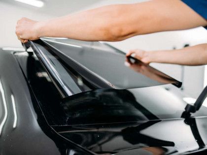 A person is applying window tinting to a black car.