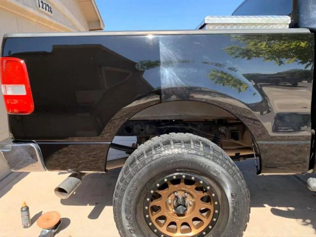 Black truck bed half polished, showing scratch removal. A tire is in front.