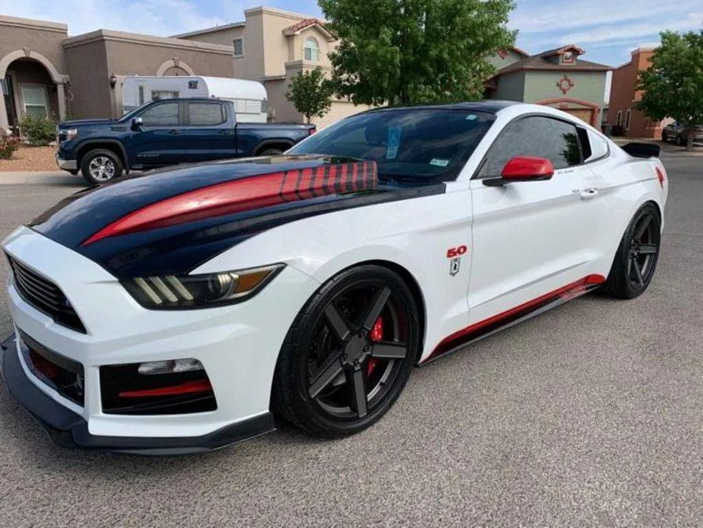 White Ford Mustang with black hood and red accents parked on a paved street.