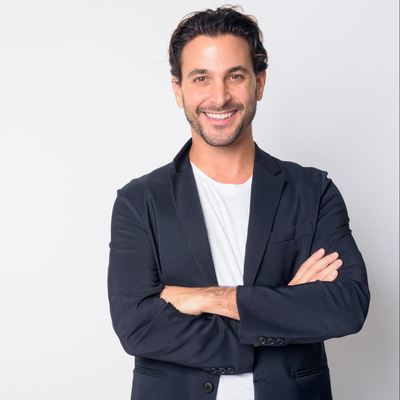 Man smiling, arms crossed, wearing a blazer over a white t-shirt. White background.