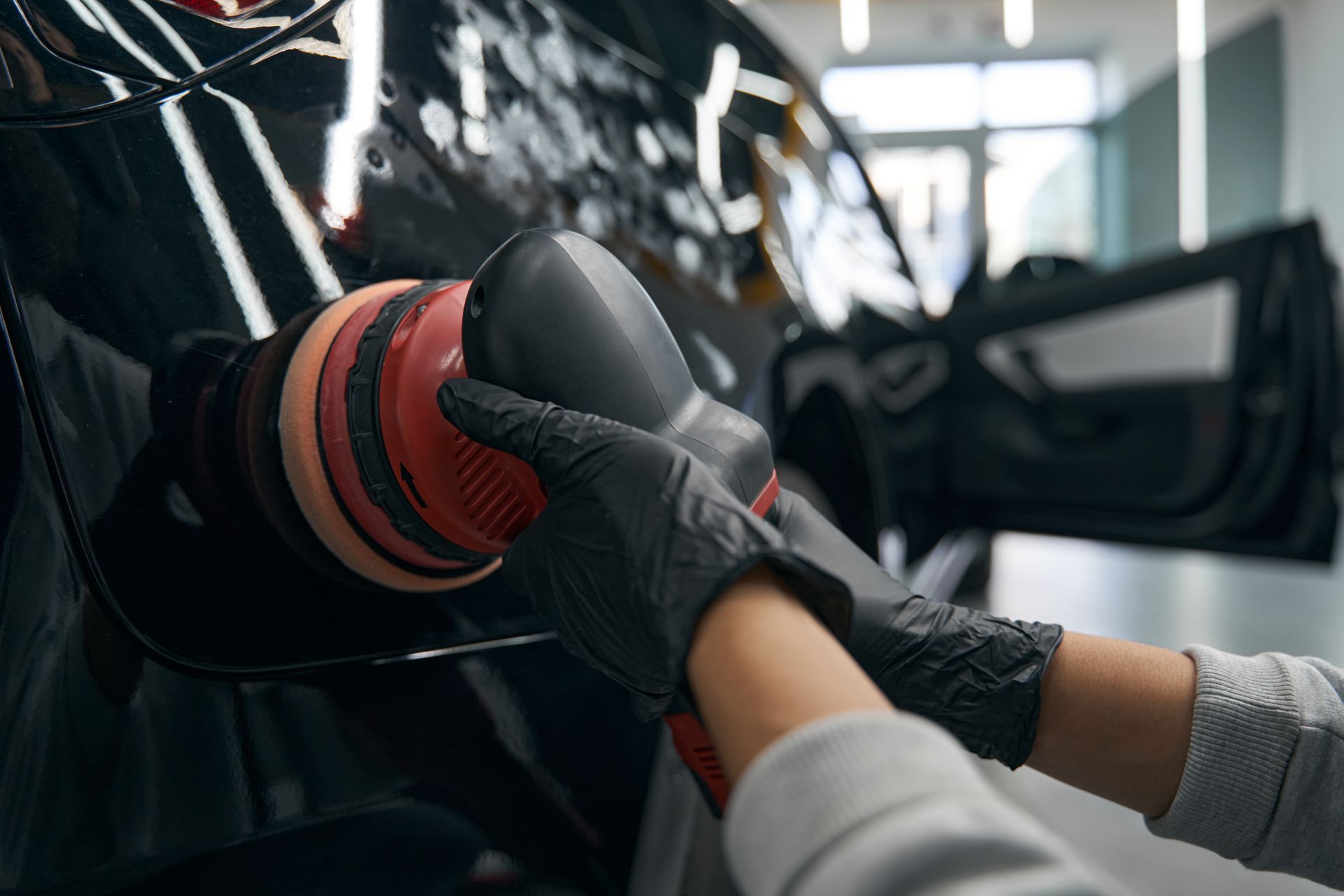 Person steam cleaning a car interior. Blue and orange gloves, steam, black car features.