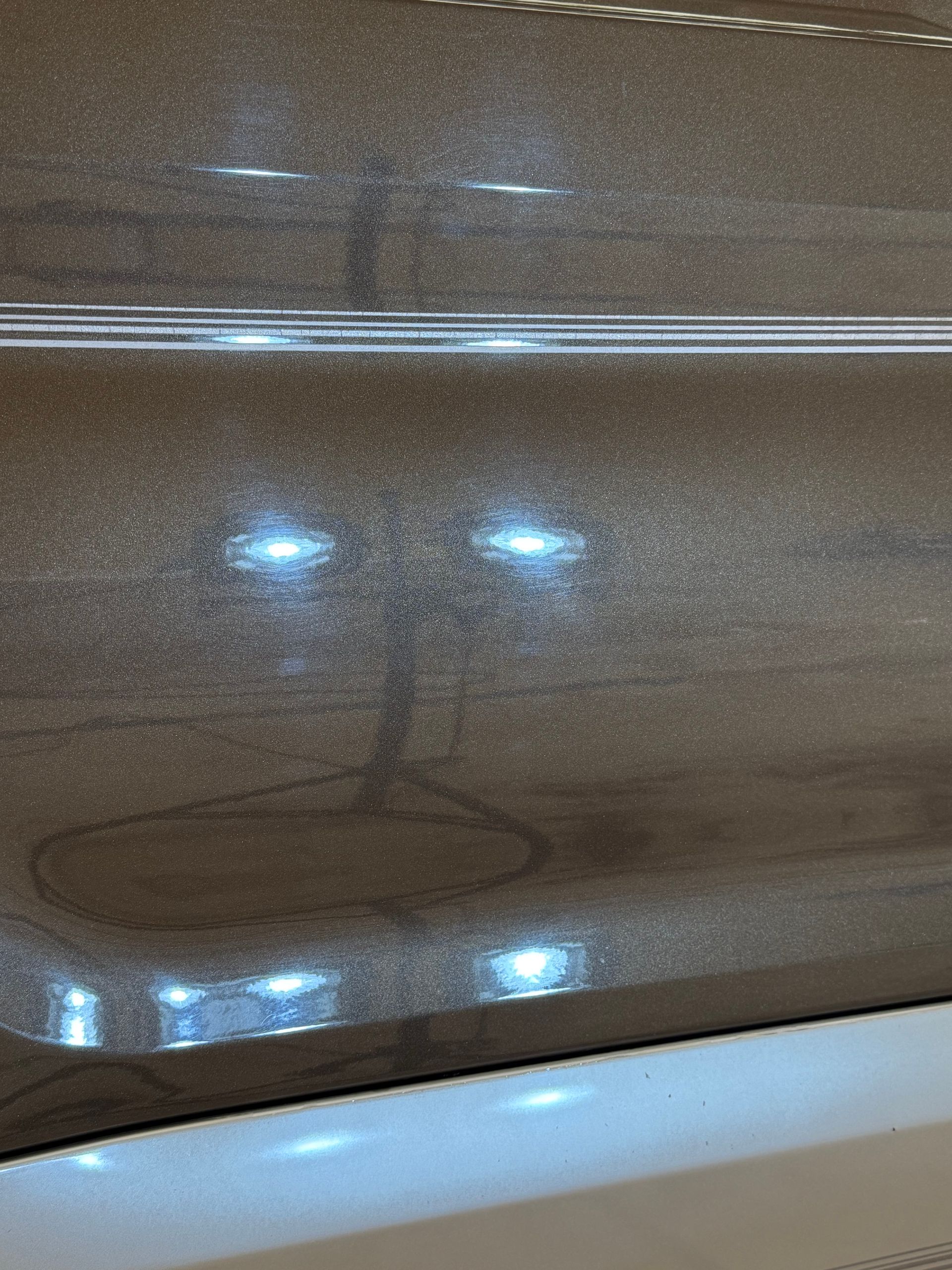 A close-up of a brown, metallic-finish surface featuring a distinct, dark circular ring mark and two bright reflections.