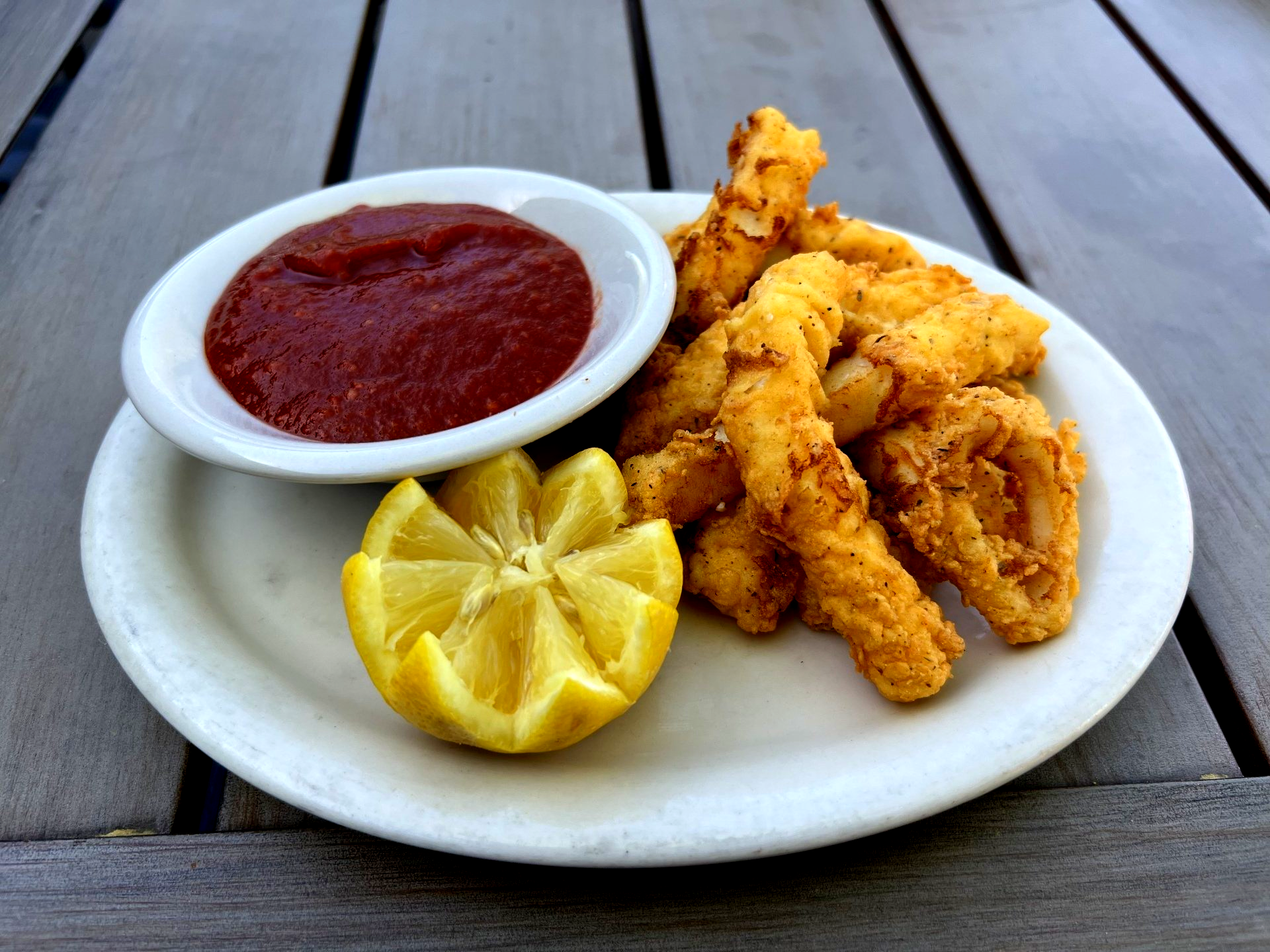 Fried food with dipping sauce and lemon wedge on a plate.