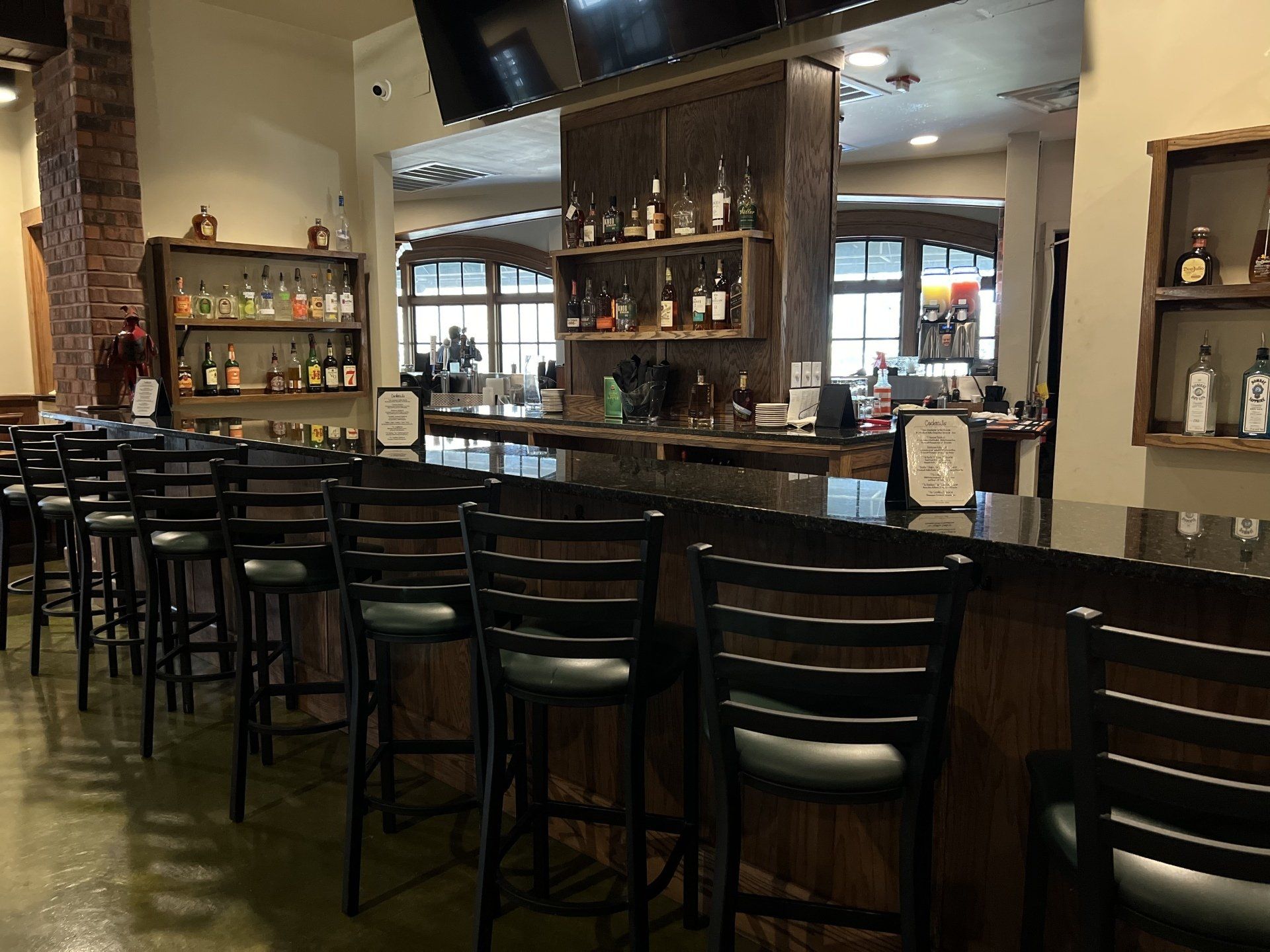 Bar with stools, shelves of liquor bottles, and a TV screen. Dark wood and stone interior.