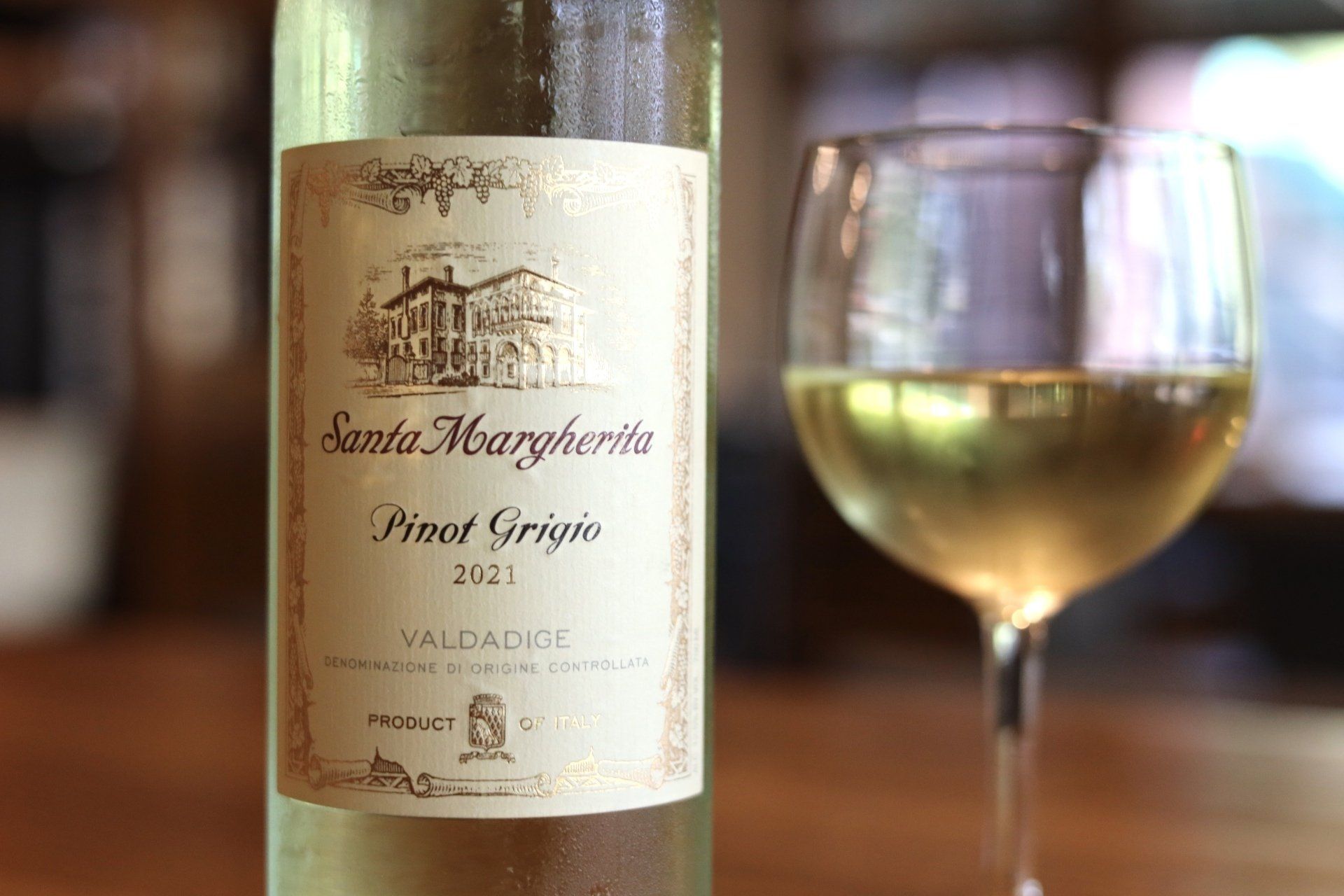 Bottle of Santa Margherita Pinot Grigio 2021 next to a wine glass with a light yellow liquid.