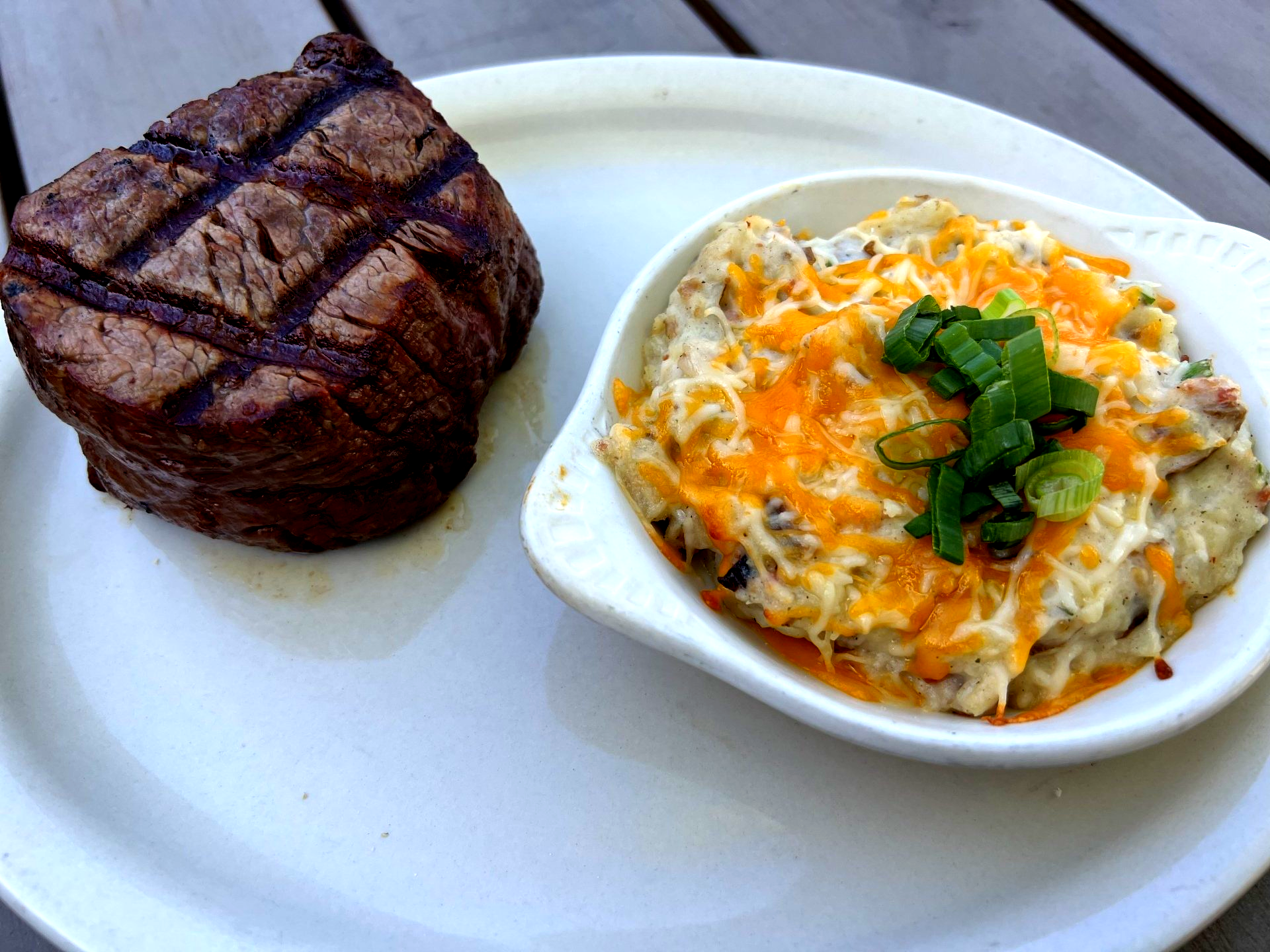 Grilled steak with side of loaded baked potato casserole, garnished with green onions.