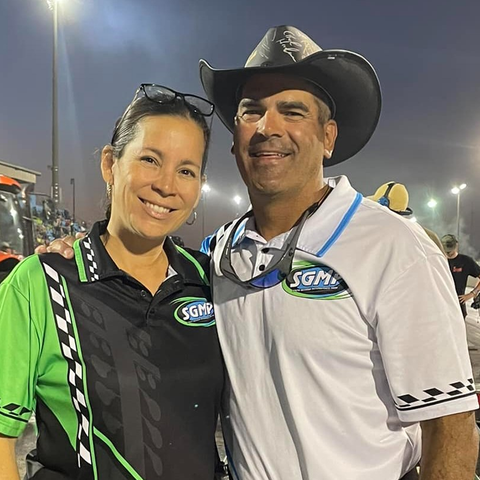 Man in cowboy hat and woman in matching shirts, smiling, at a racetrack.