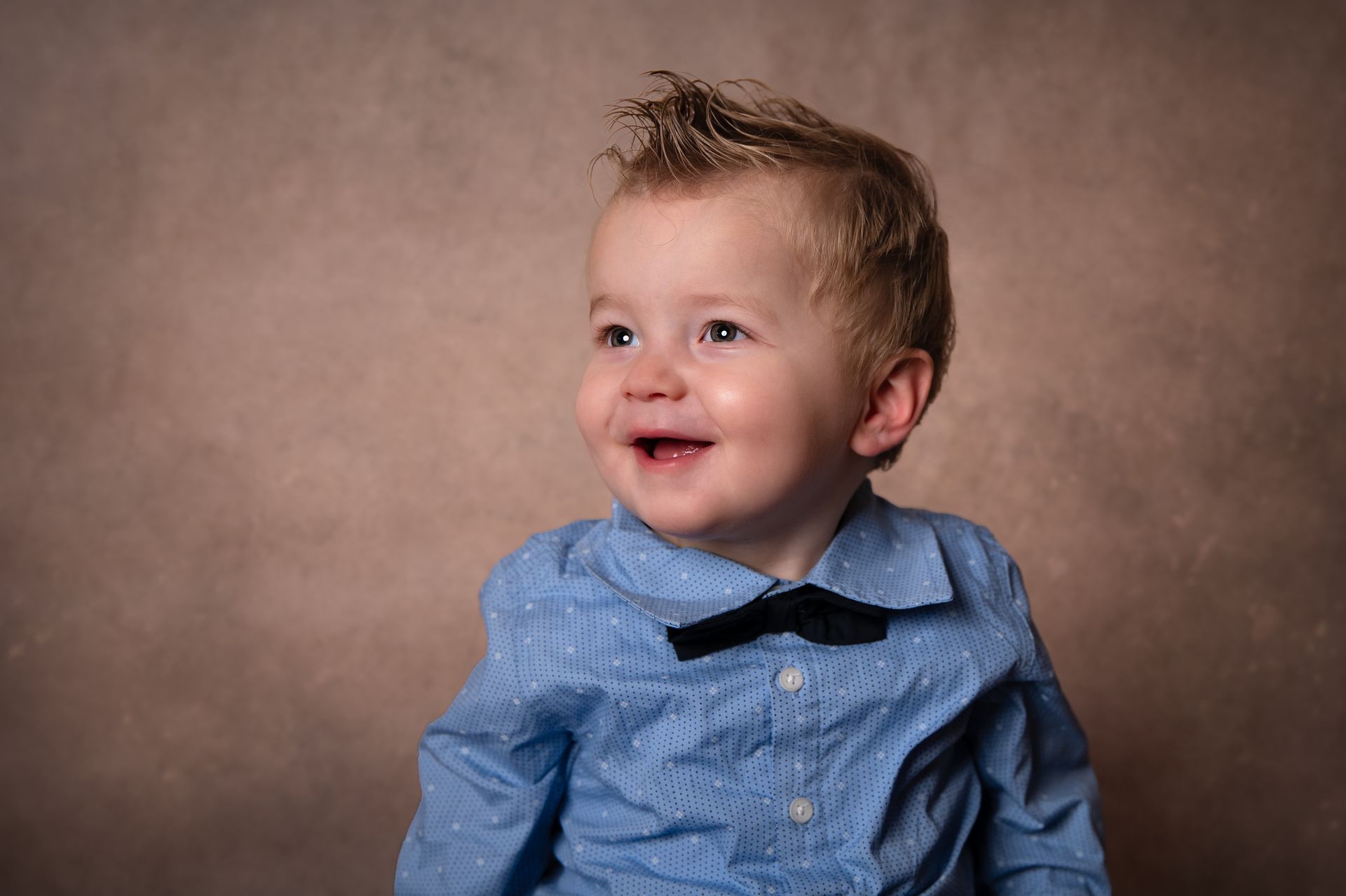 Een jonge jongen draagt ​​een blauw overhemd en een vlinderdas en lacht.