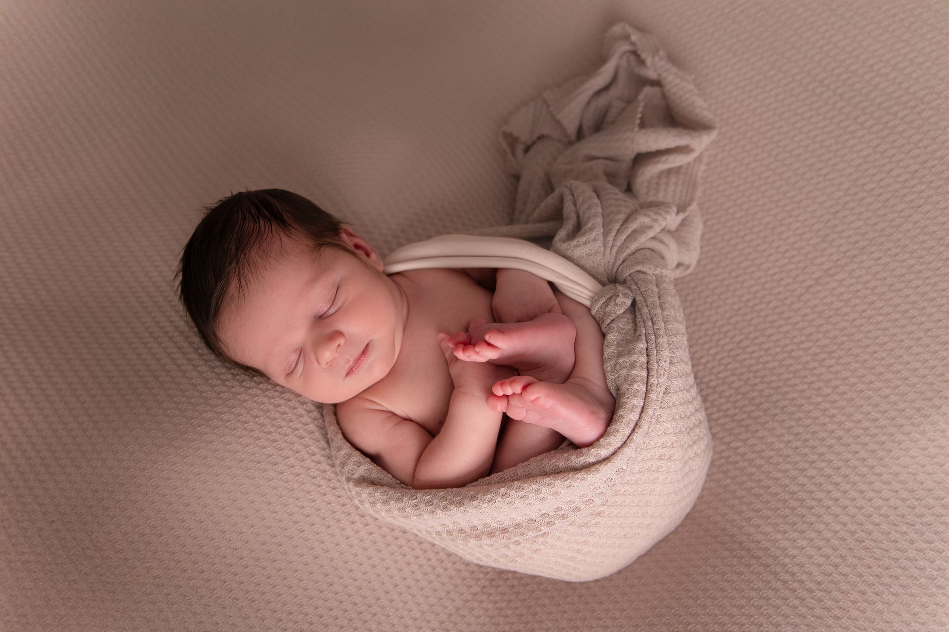 Een pasgeboren baby, gewikkeld in een deken, slaapt op een bed.