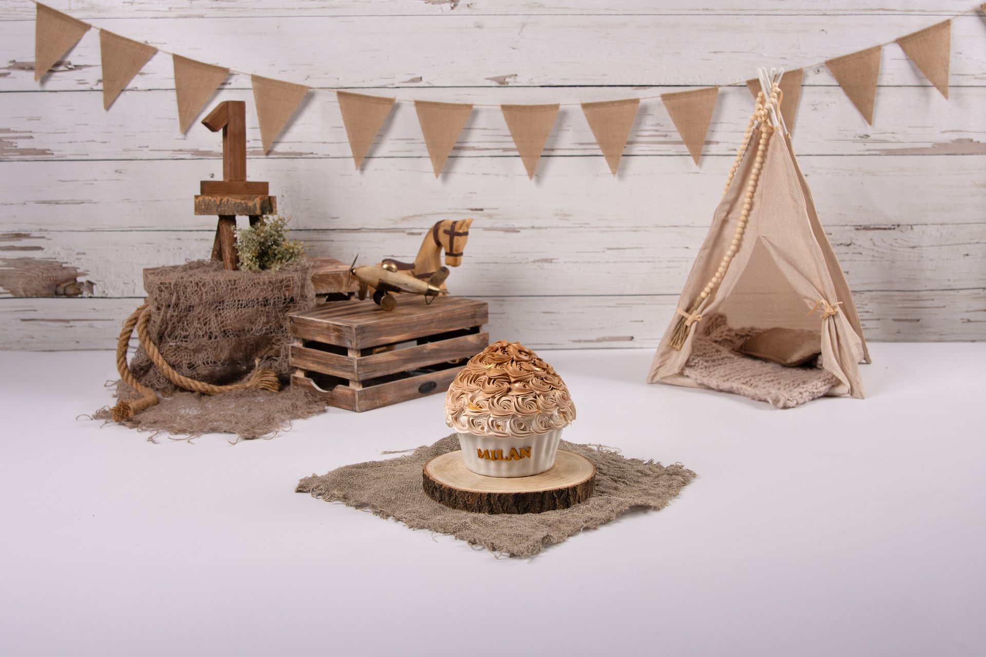 Een cupcake staat op een houten tafel naast een tipi en een schommelpaard.