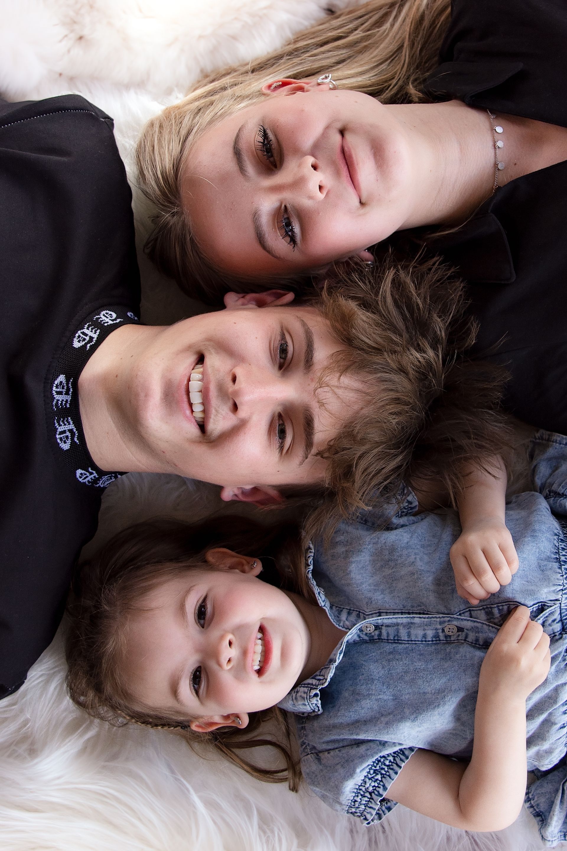 Drie mensen liggen op een wit, pluizig oppervlak: een lachende jonge vrouw, een lachende jongere man en een klein kind dat naar boven lacht.