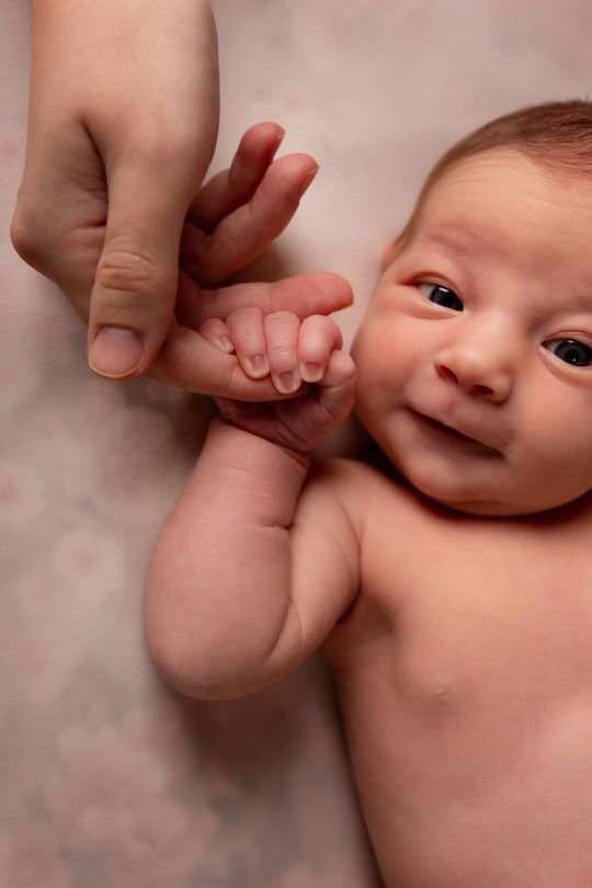 Een close-up van een persoon die de hand van een baby vasthoudt.