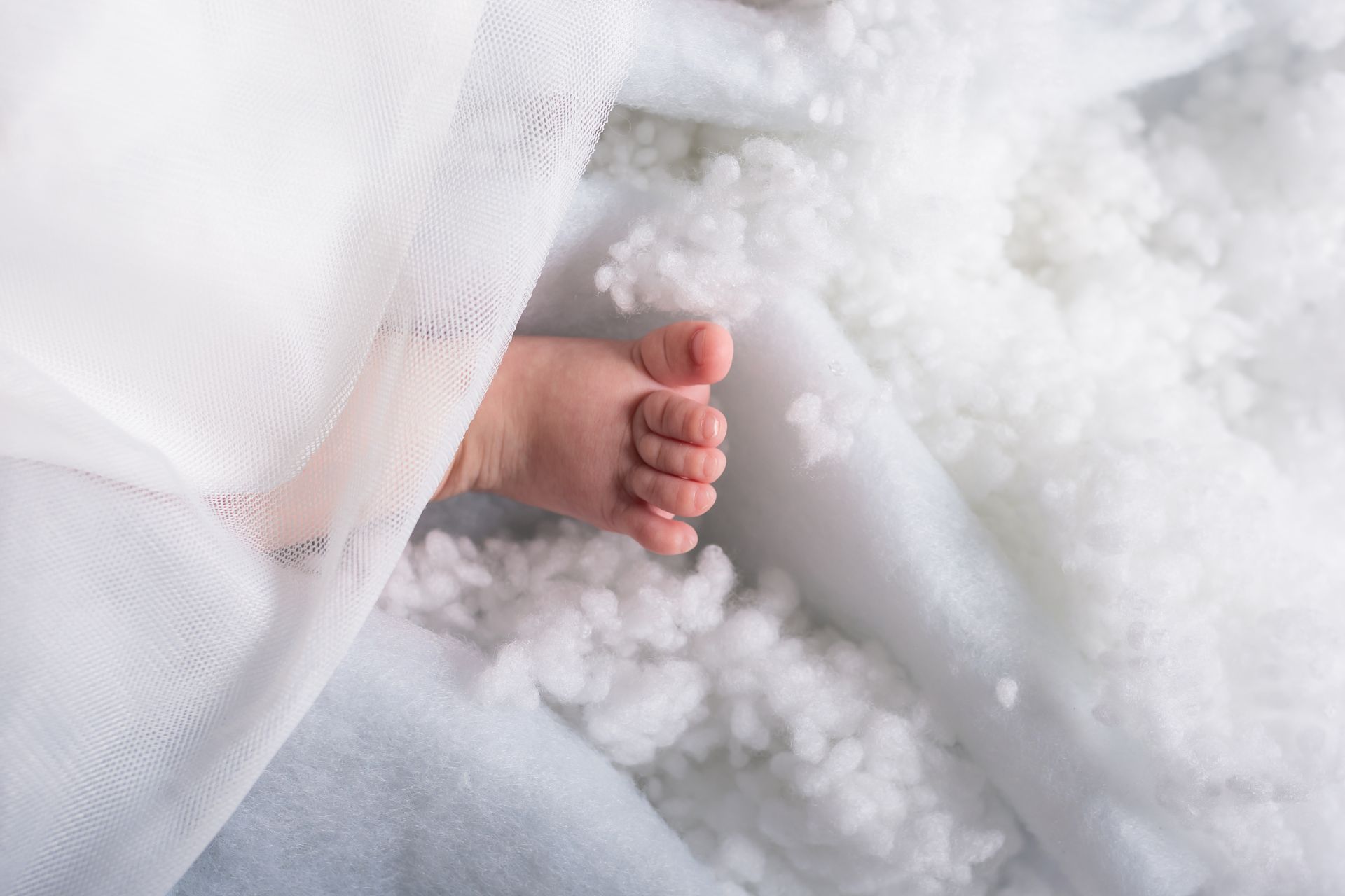 Een babyvoetje steekt uit een witte deken.