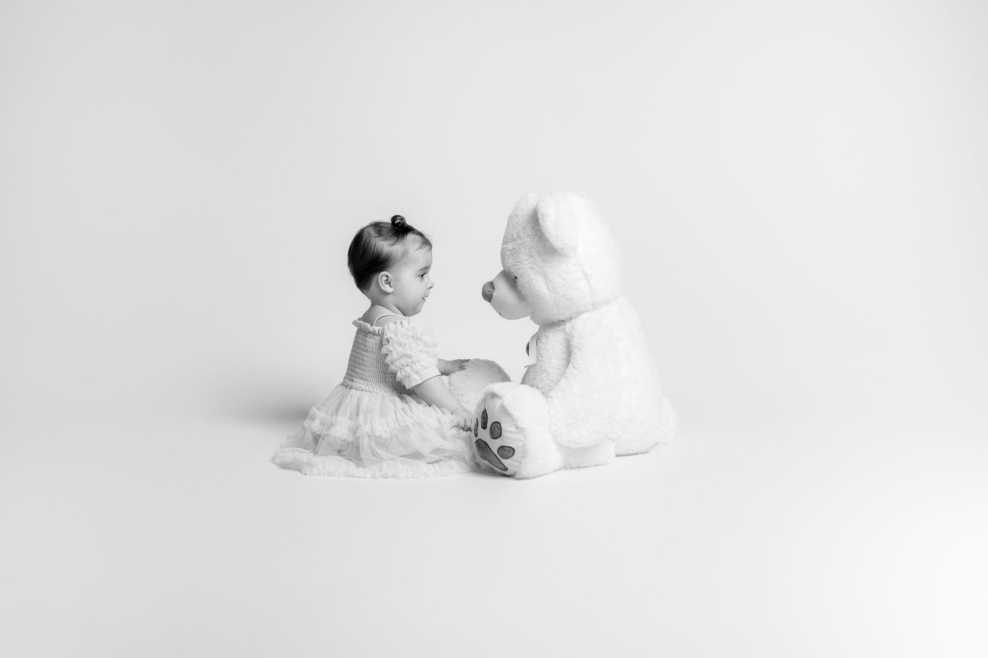 Een baby zit naast een witte teddybeer.