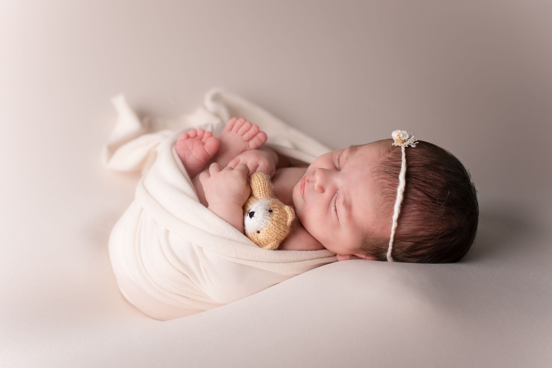 Een pasgeboren baby is gewikkeld in een witte deken en houdt een teddybeer vast.