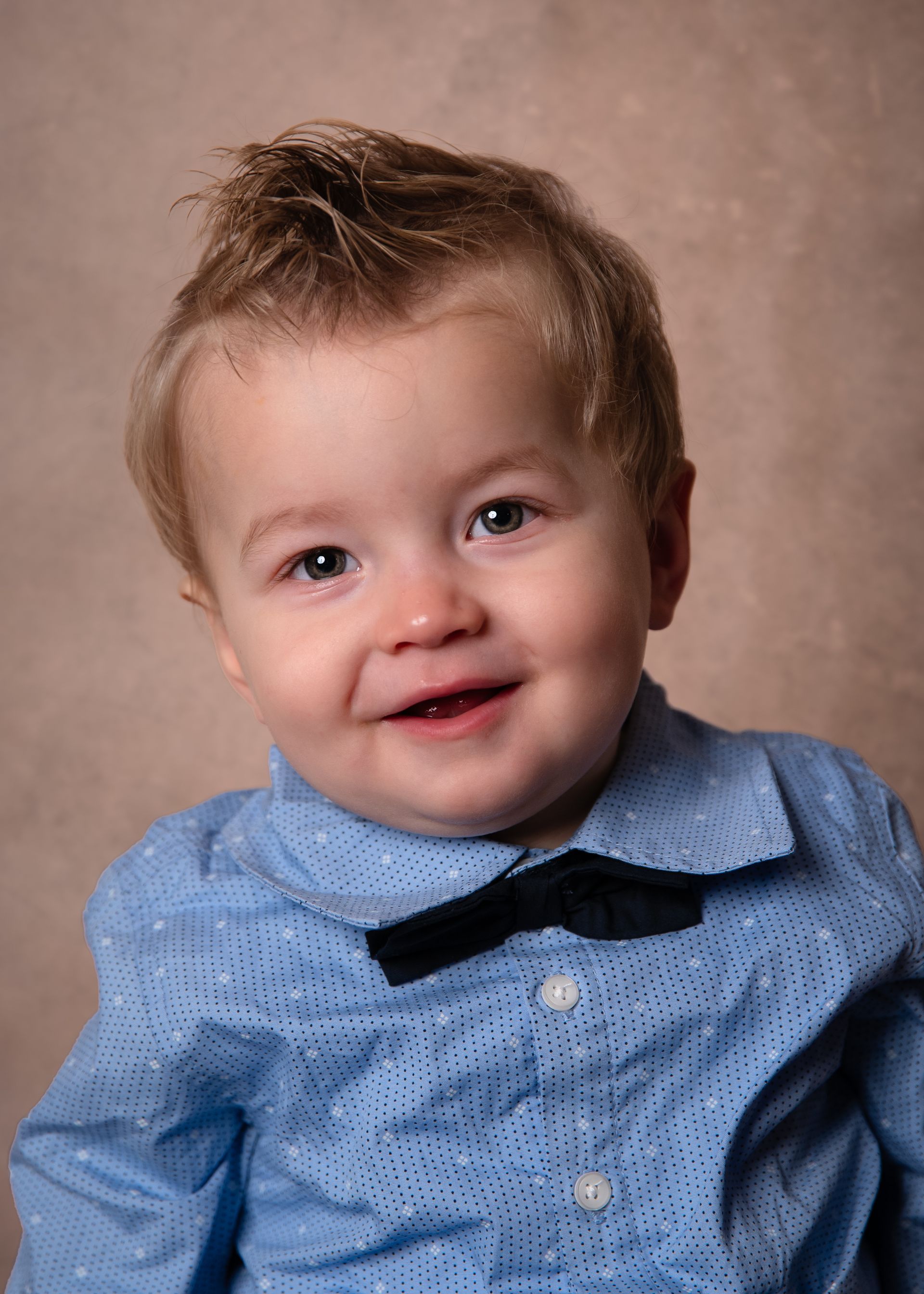 Een jonge jongen draagt ​​een blauw overhemd en een vlinderdasje en lacht naar de camera.