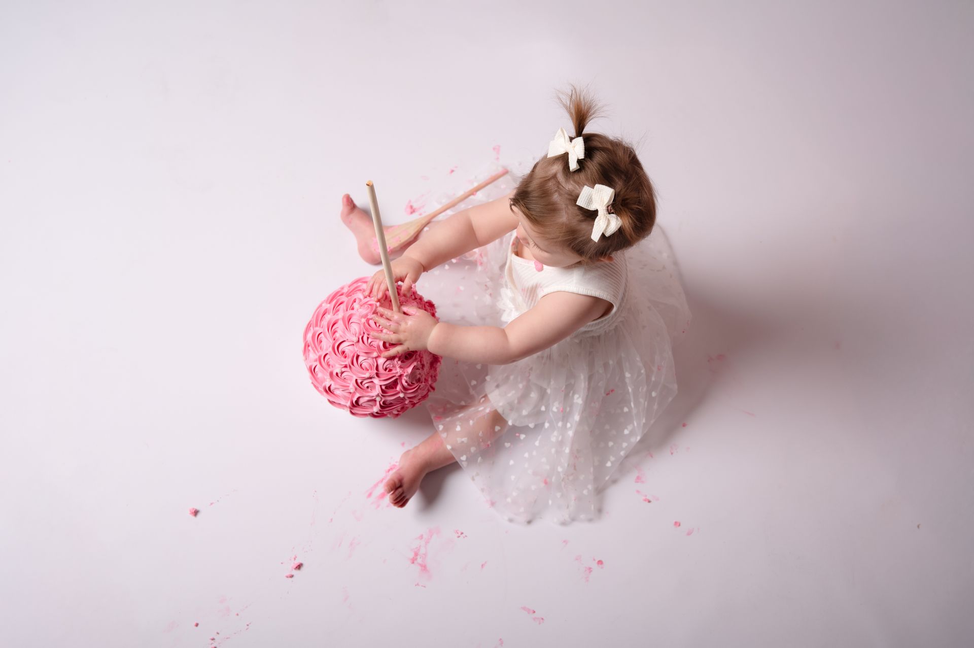 Een klein meisje zit op de grond en eet een roze taart.