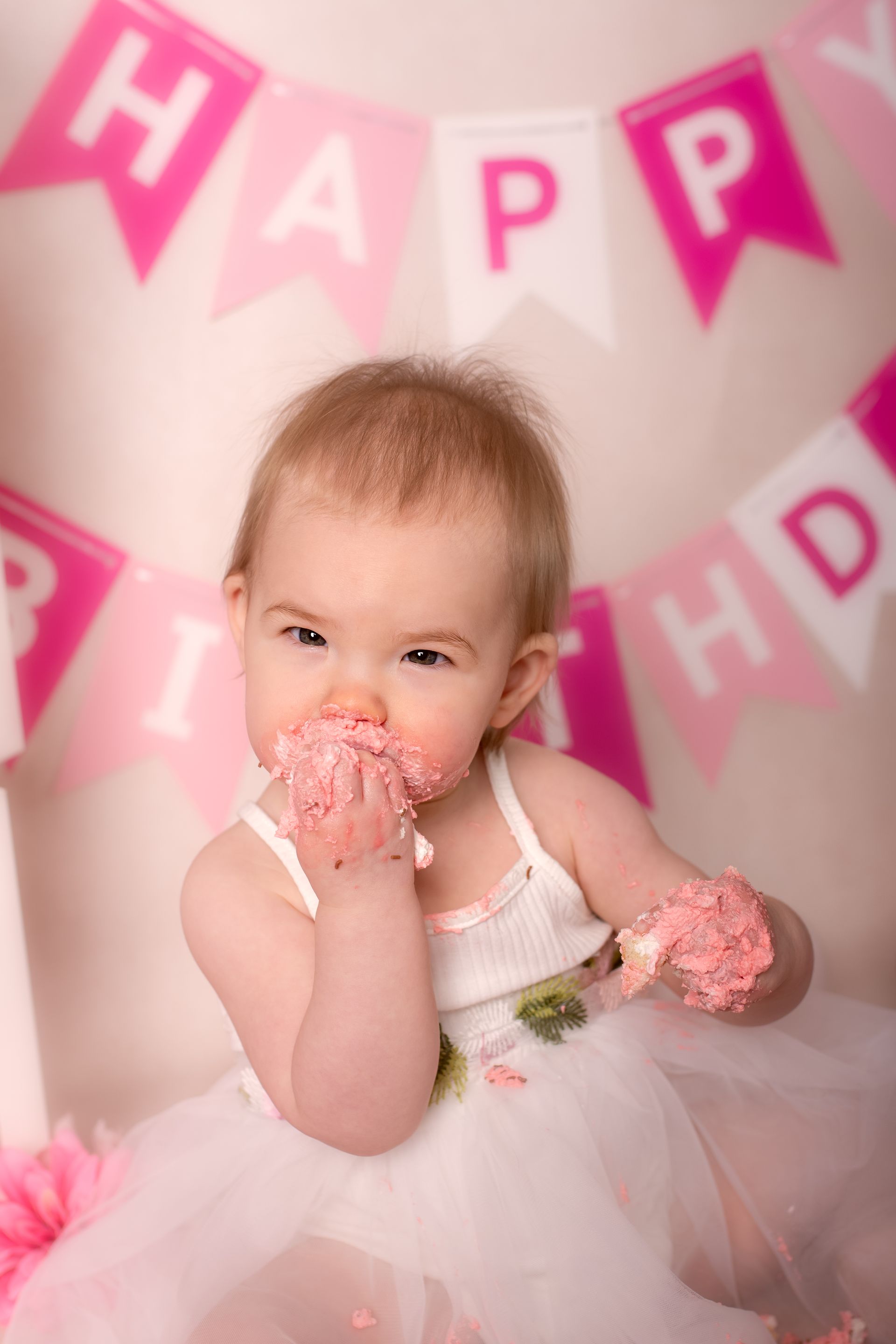 Een babymeisje eet een cupcake voor een spandoek met de tekst 'Happy Birthday'.