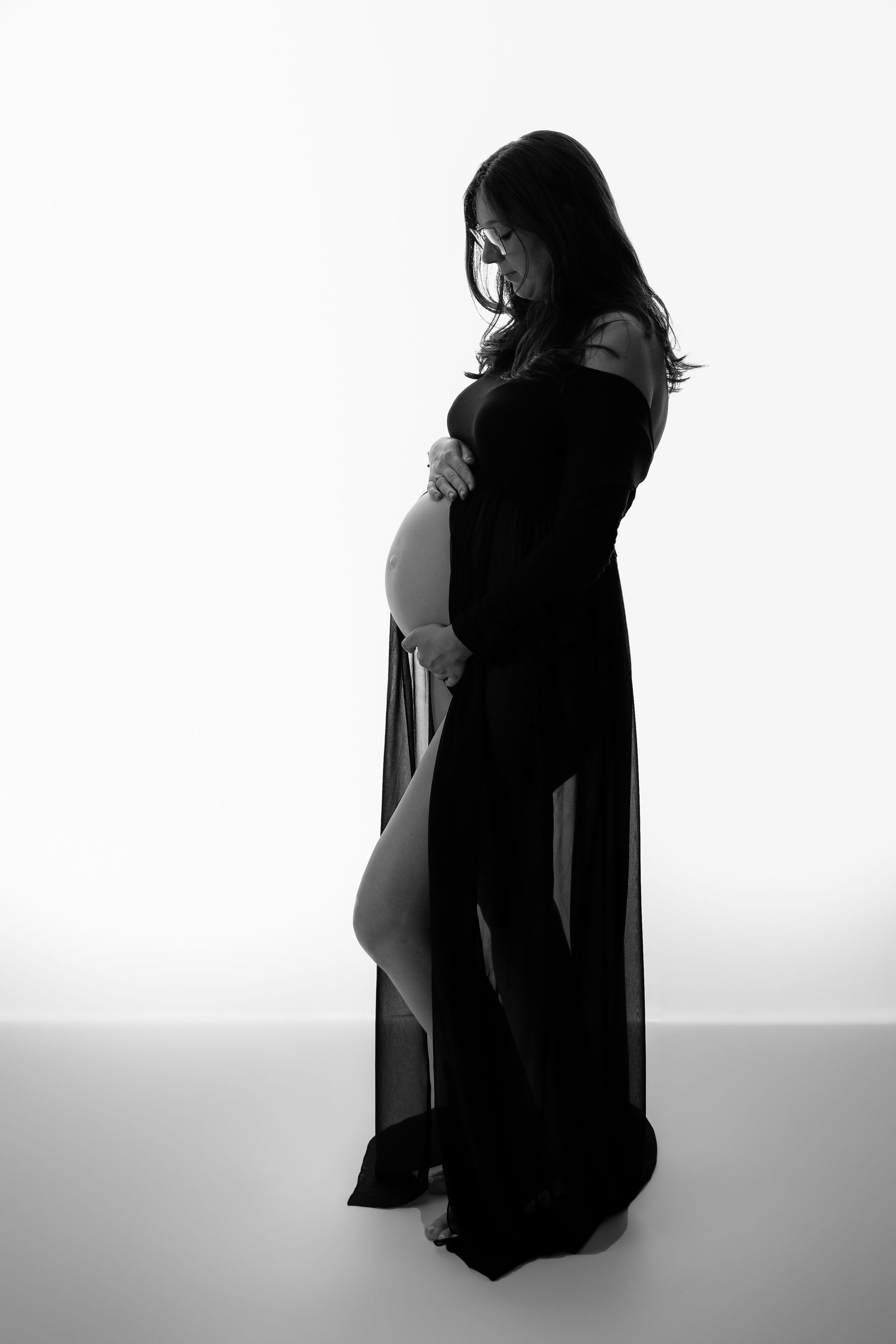 Een zwart-witfoto van een zwangere vrouw in een lange zwarte jurk die haar buik vasthoudt.