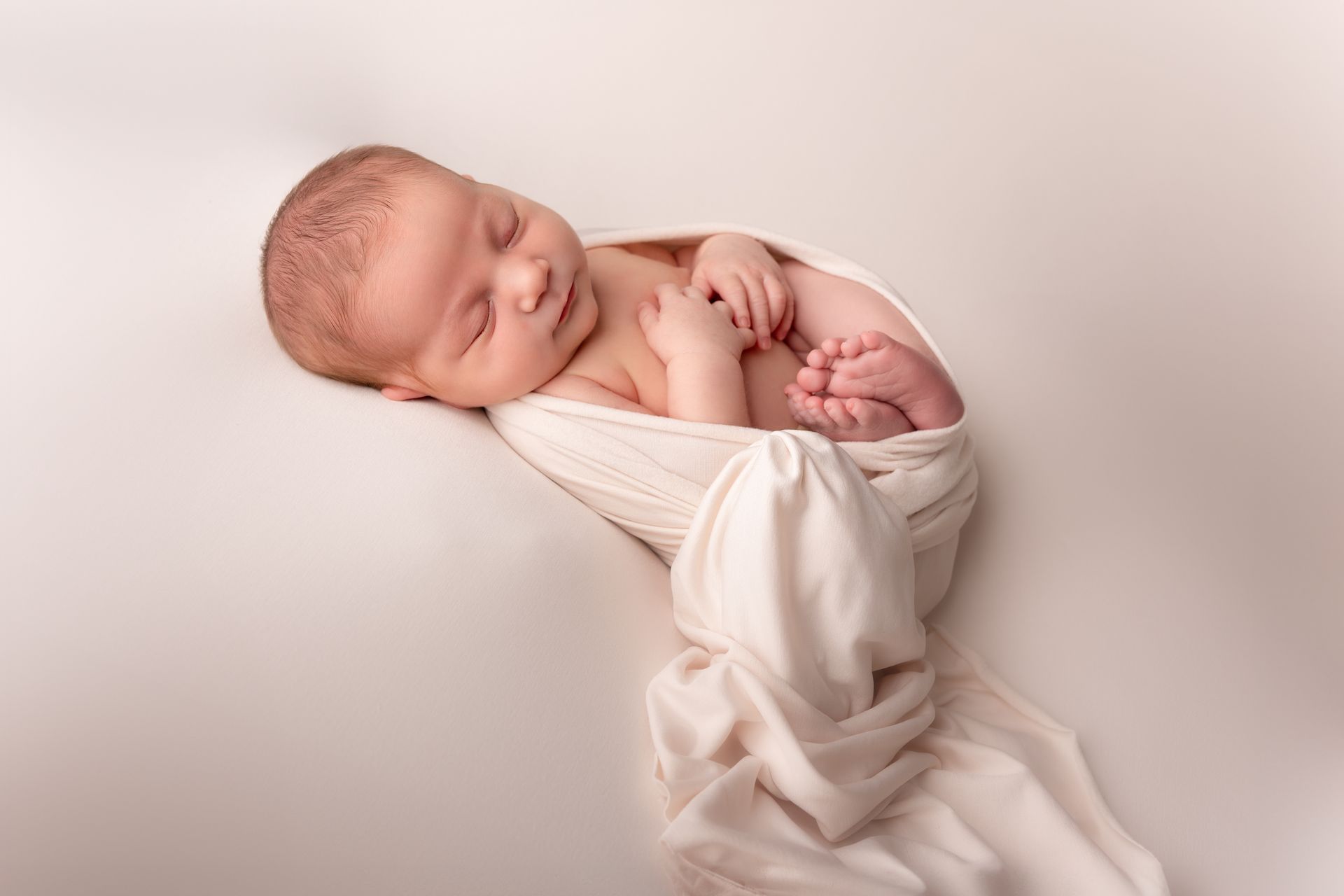 Een pasgeboren baby, gewikkeld in een witte deken, slaapt op een wit oppervlak.