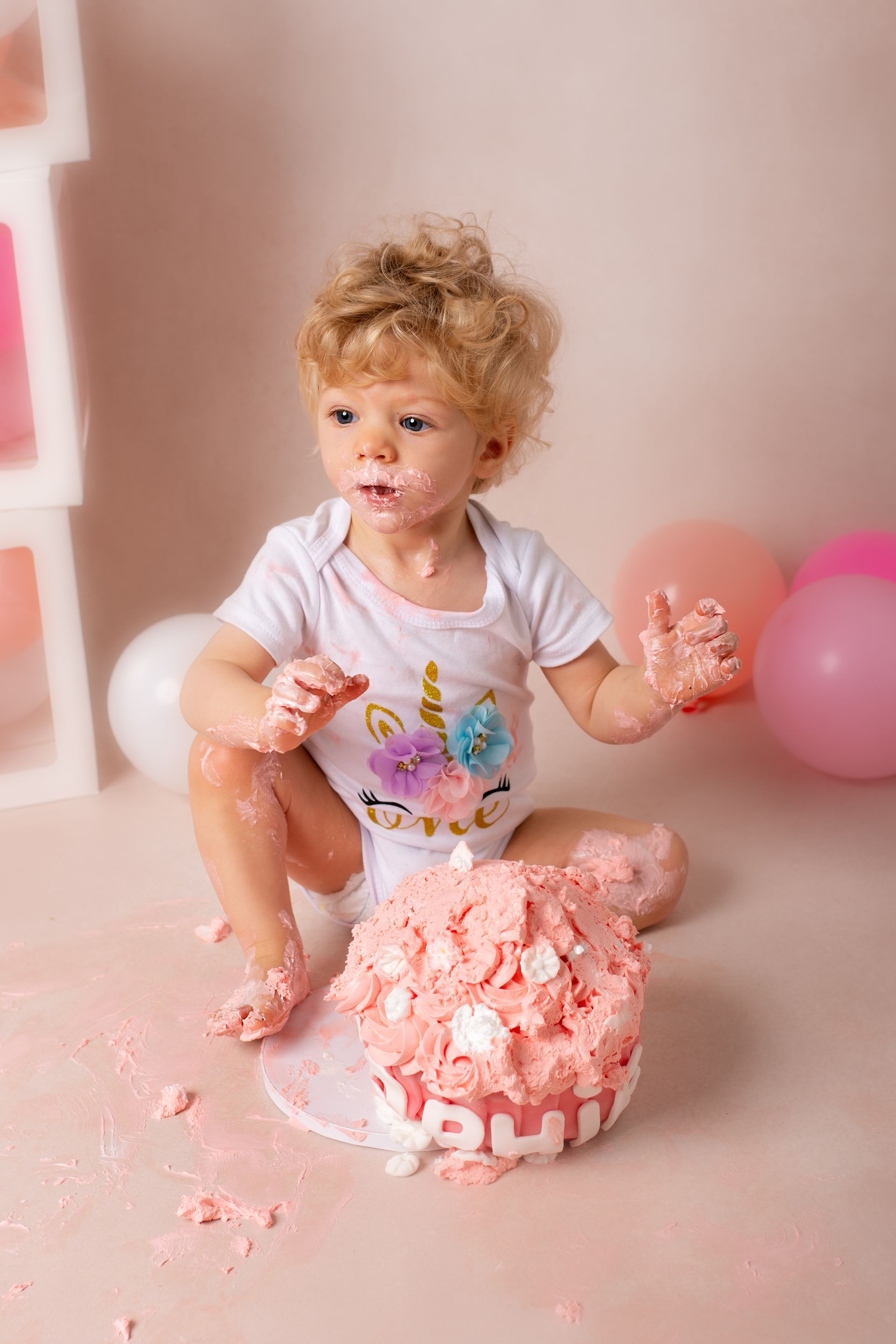 Een baby zit op de grond en eet een roze taart.