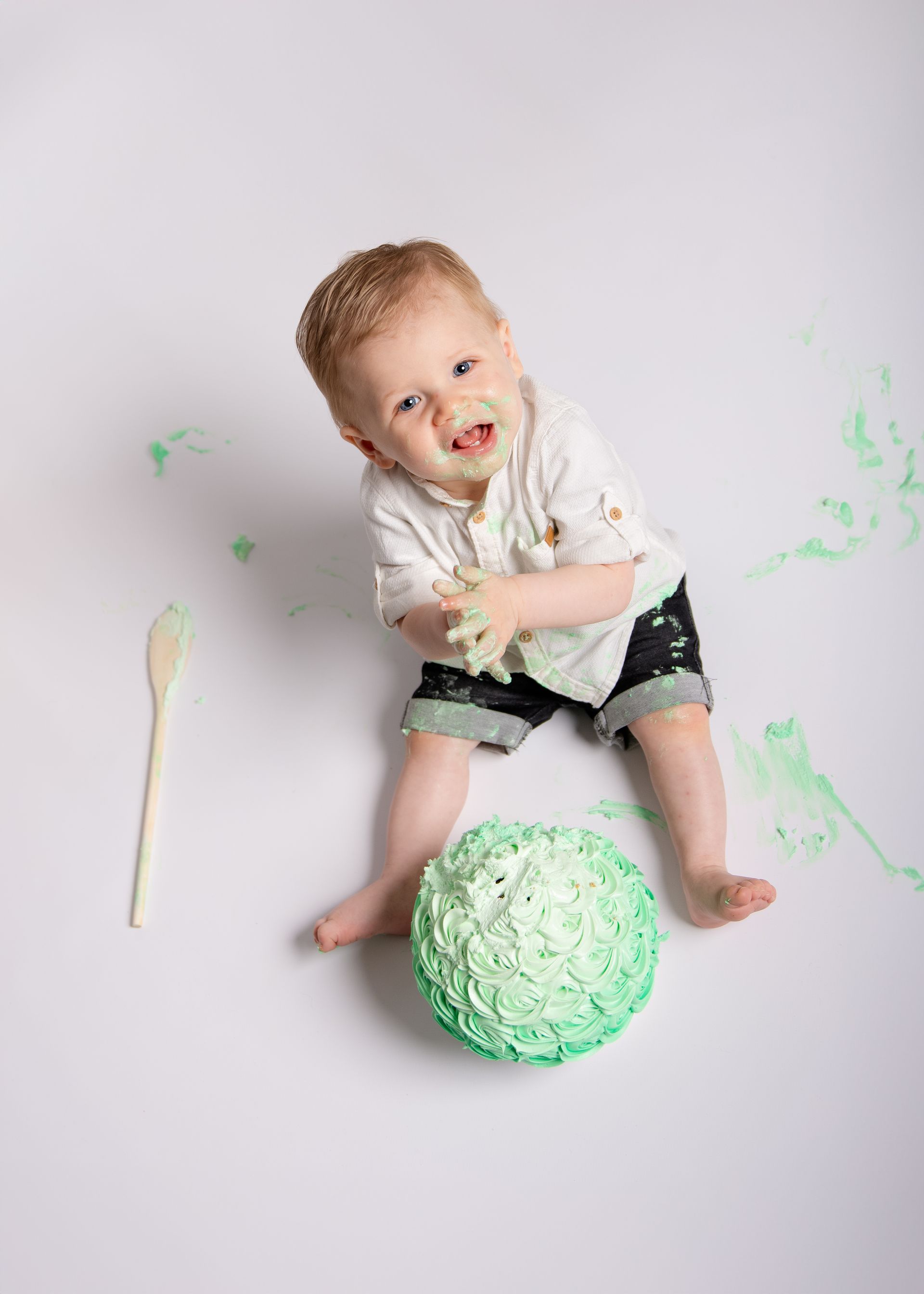 Een baby zit op de grond met een taart en een lepel.