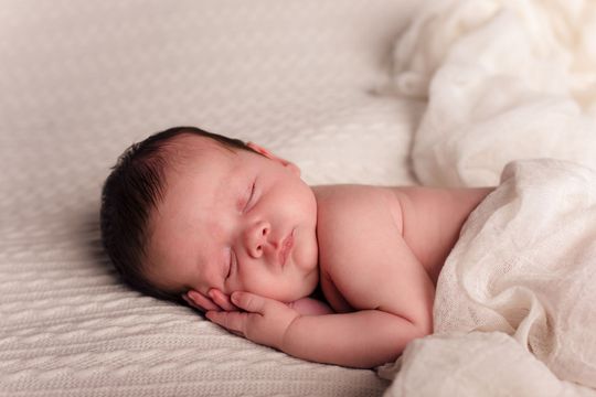 Een pasgeboren baby slaapt op een bed, gewikkeld in een witte deken.