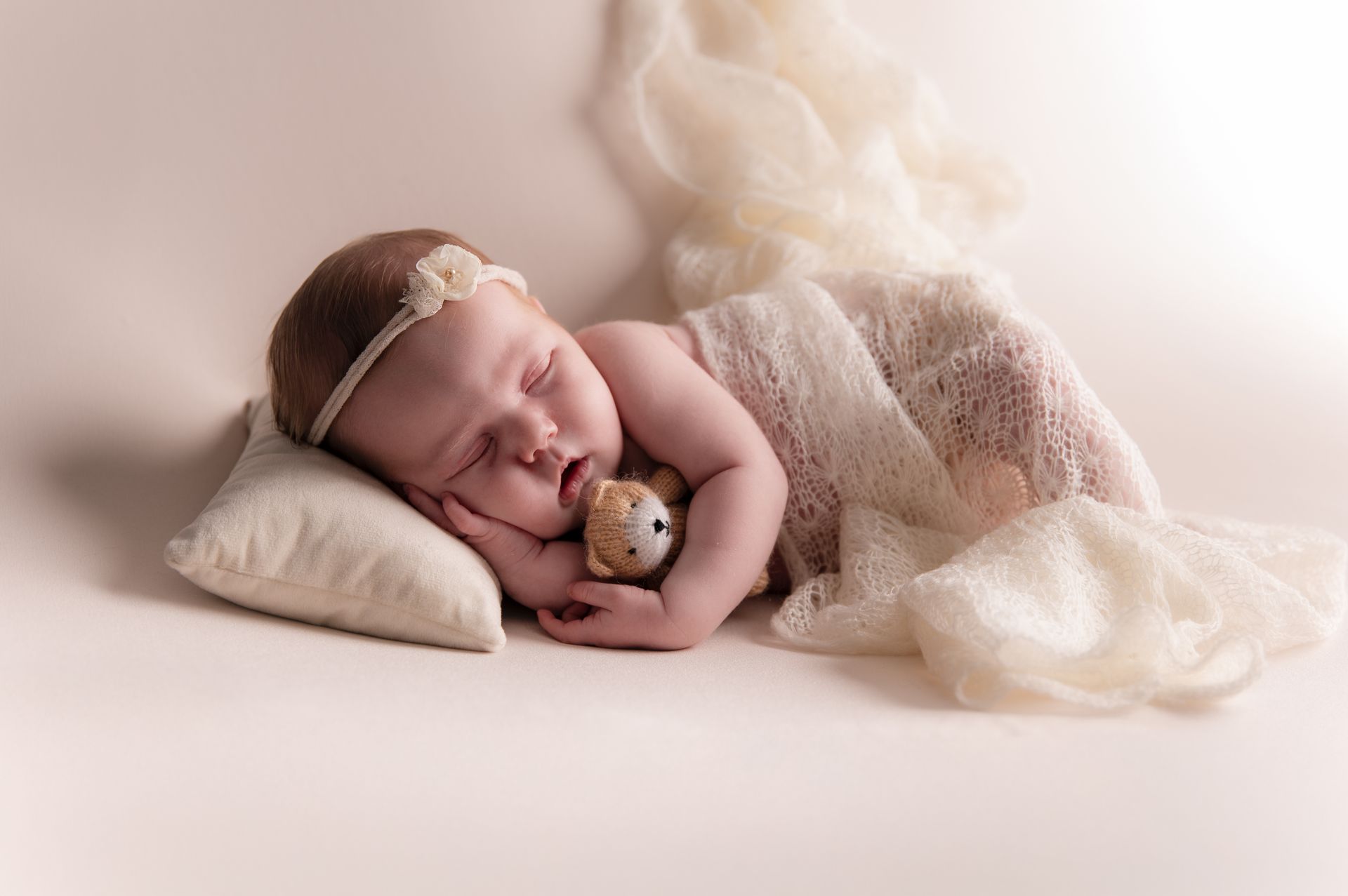 Een pasgeboren baby slaapt op een kussen met een teddybeer in haar mond.