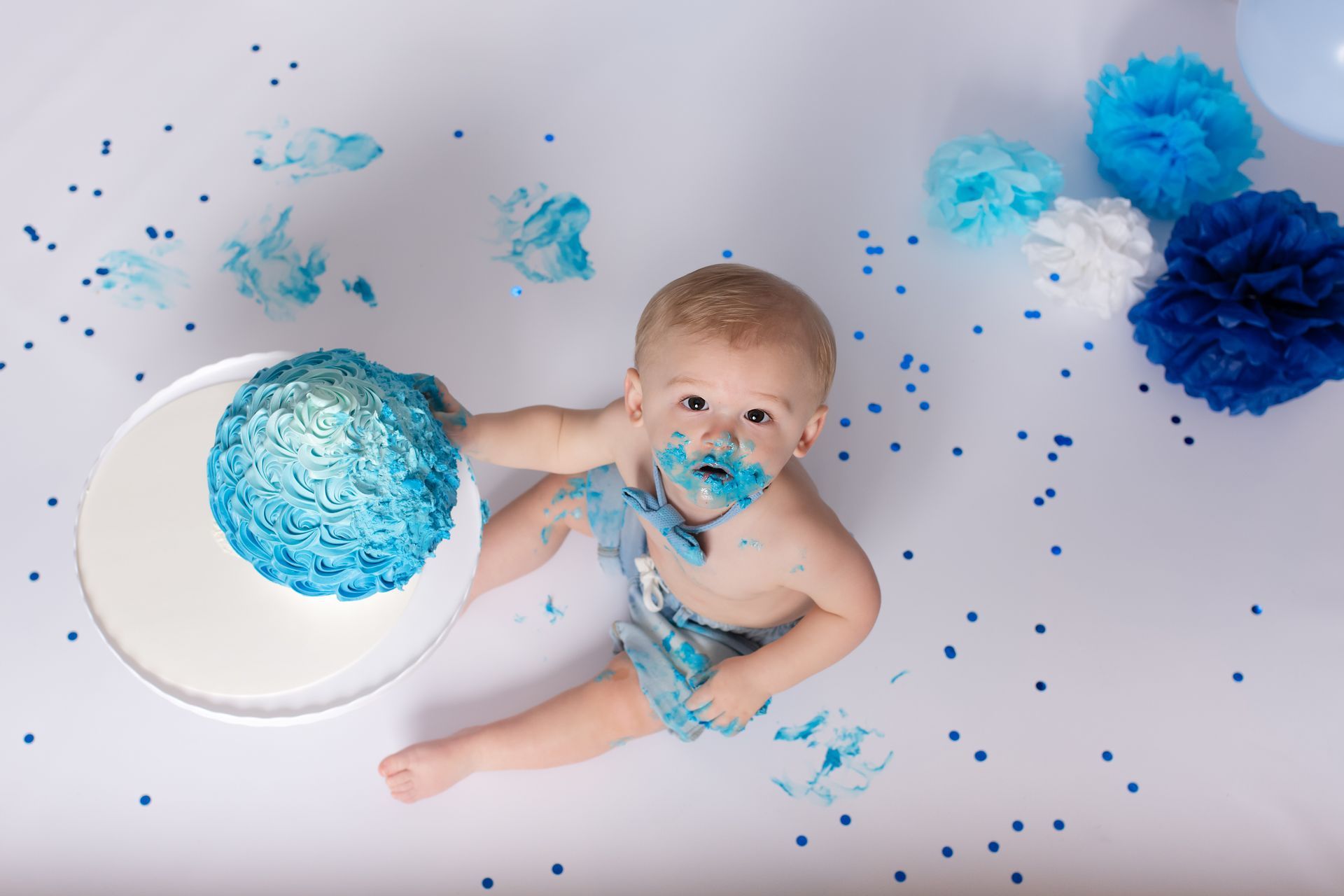 Een baby eet een blauwe taart terwijl hij op de grond ligt.