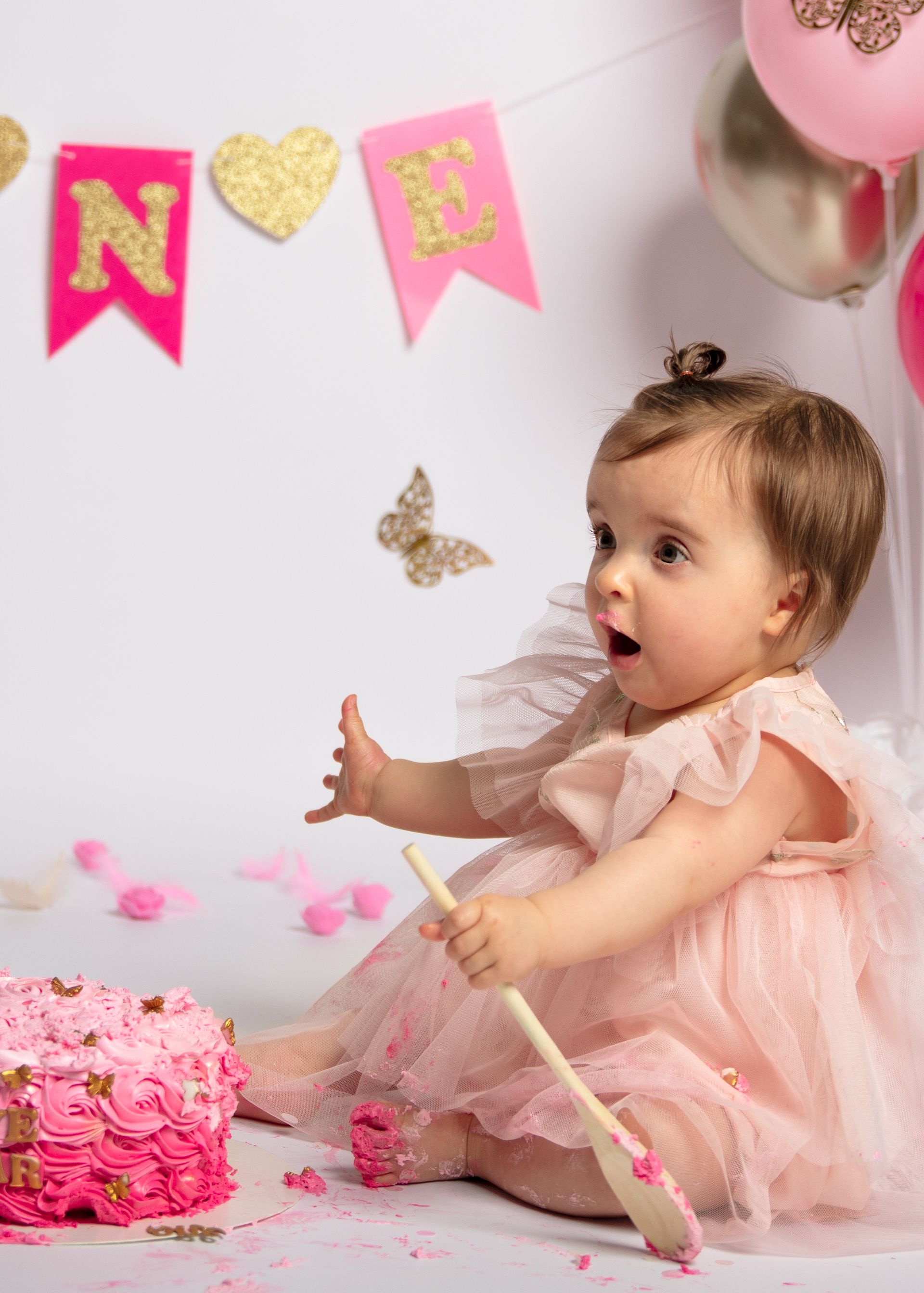 Een babymeisje zit op een tafel met een taart en een lepel.