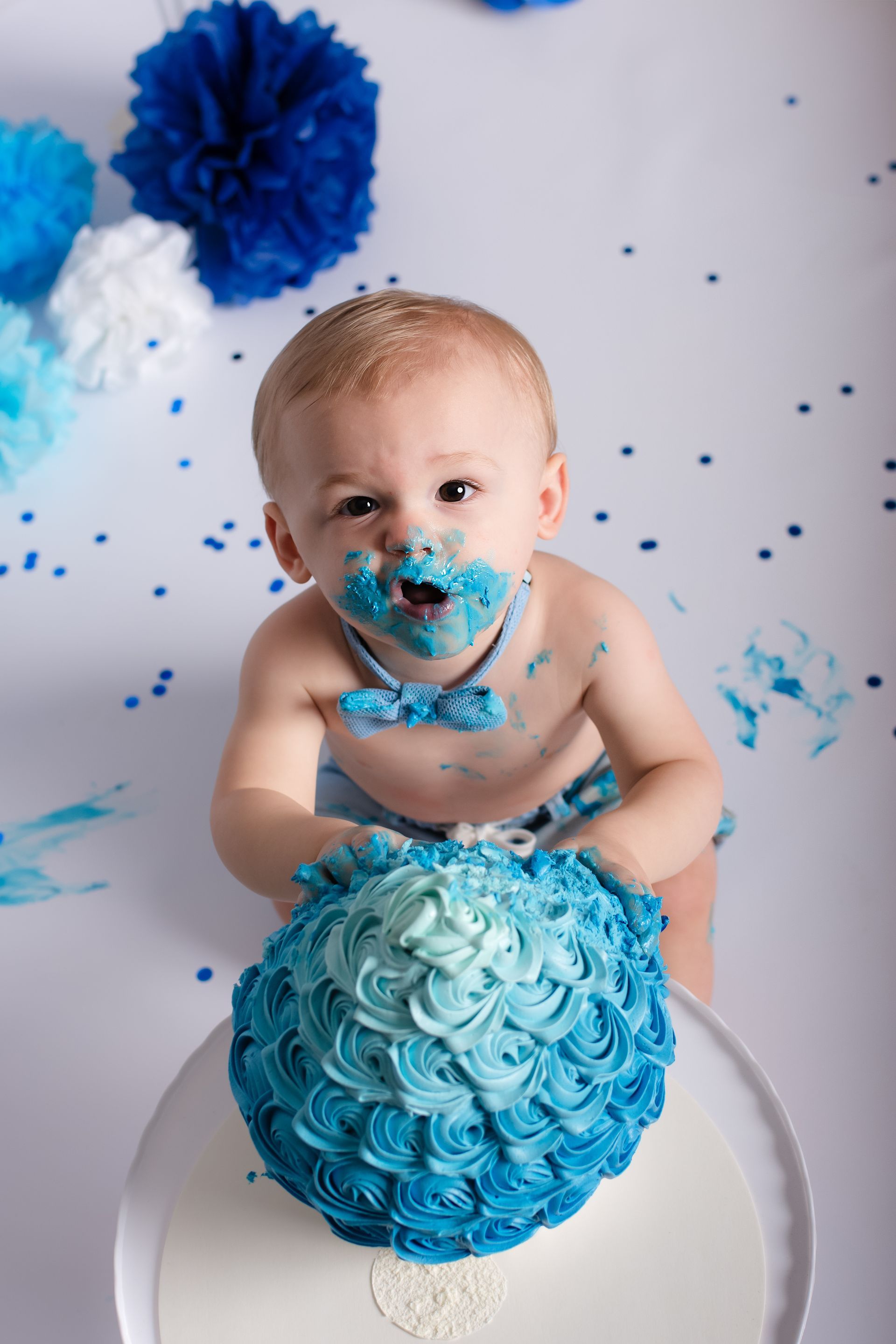 Een baby zit op een taart met blauwe glazuur op zijn gezicht.