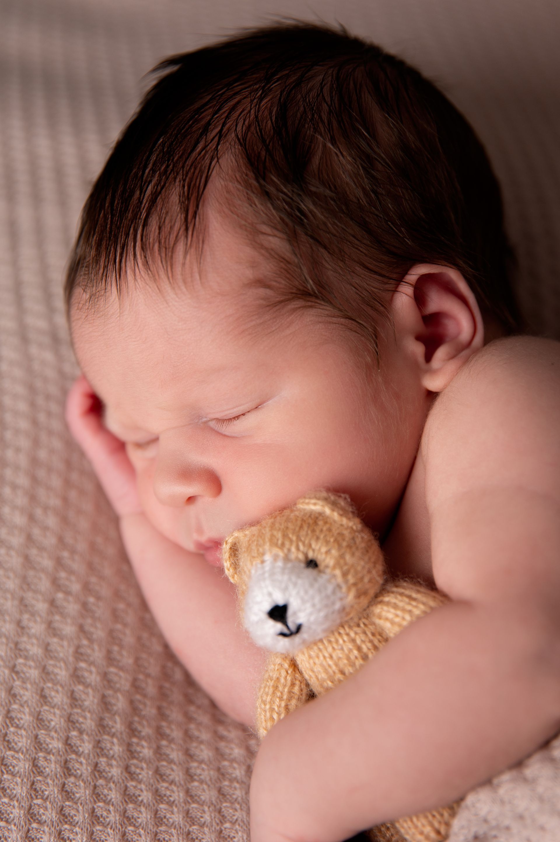 Een pasgeboren baby slaapt met een teddybeer in zijn armen.