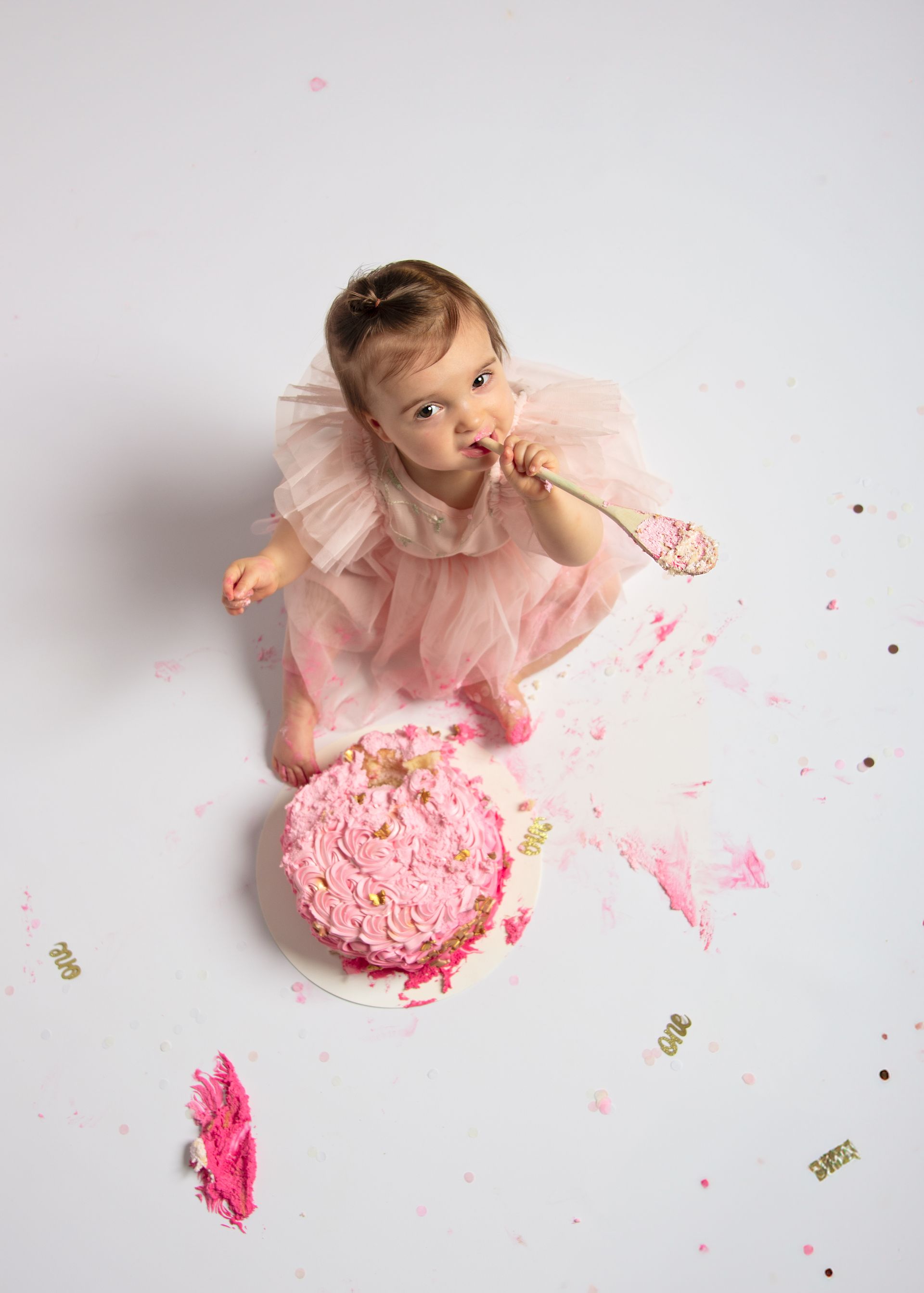 Een babymeisje eet een roze taart met een lepel.