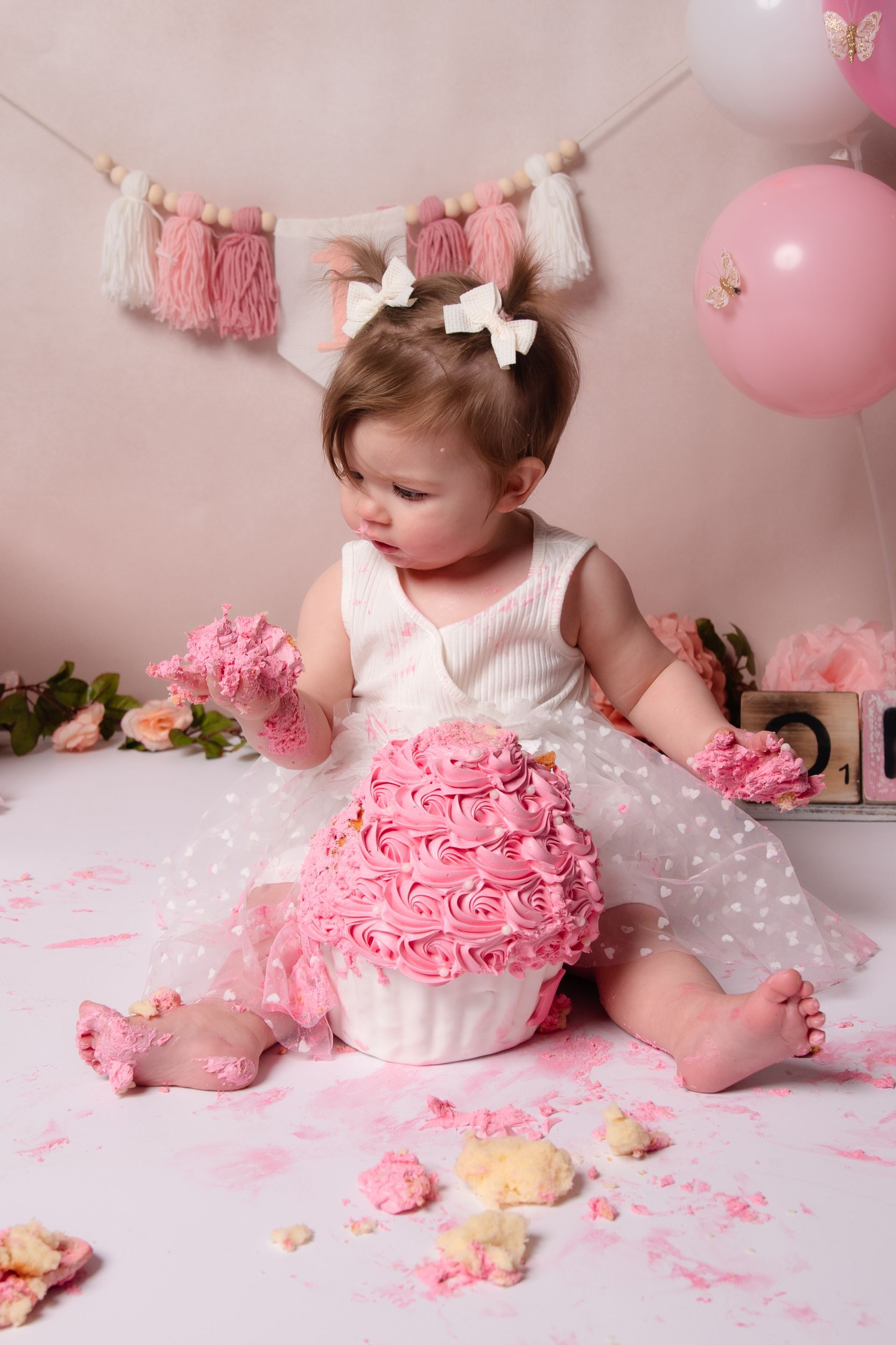Een babymeisje zit naast een gigantische cupcake bedekt met roze glazuur.