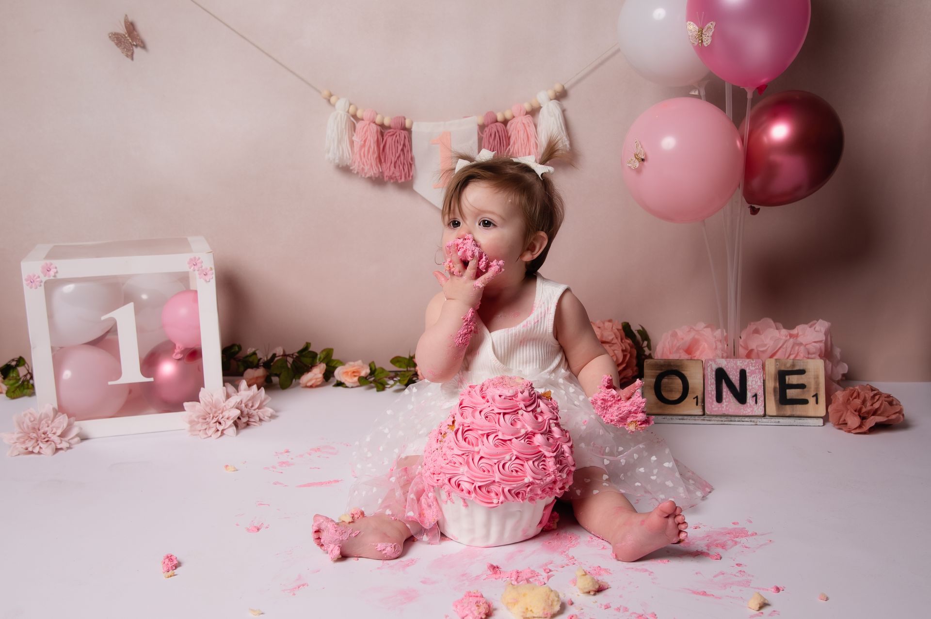 Een babymeisje zit op een tafel en eet een roze taart.