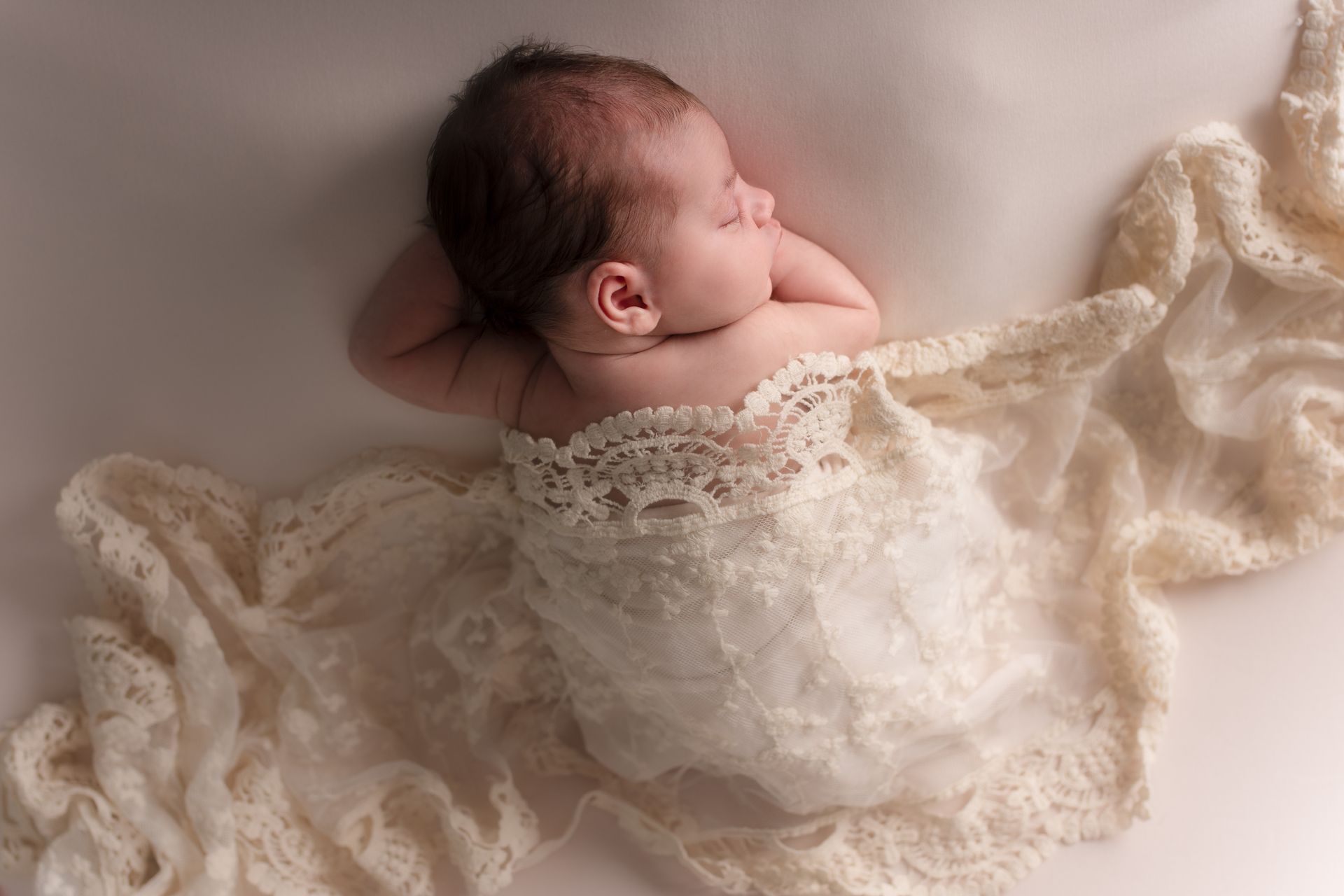Een pasgeboren baby is gewikkeld in een witte kanten deken.