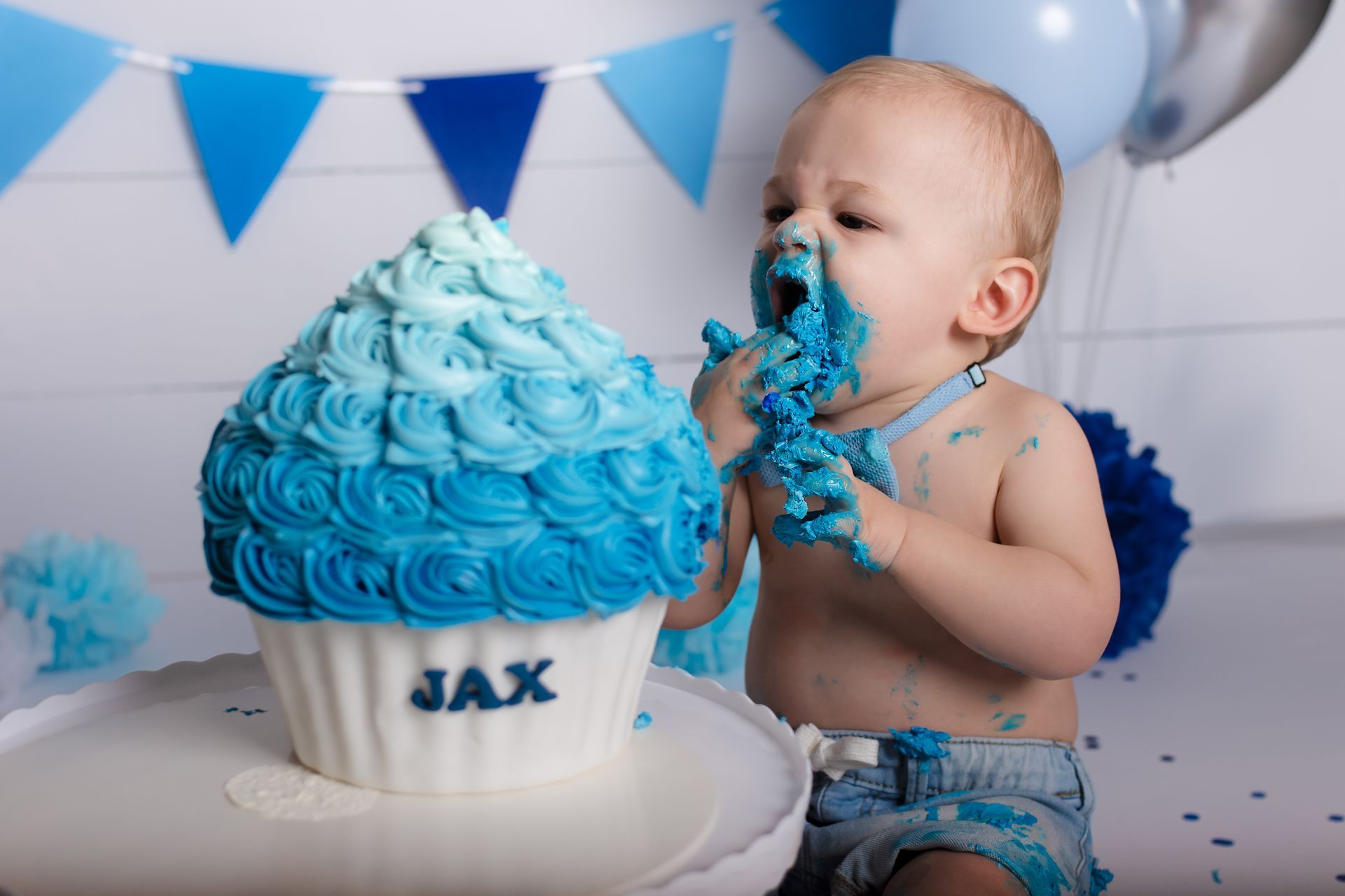 Een baby eet een gigantische cupcake met blauwe glazuur.