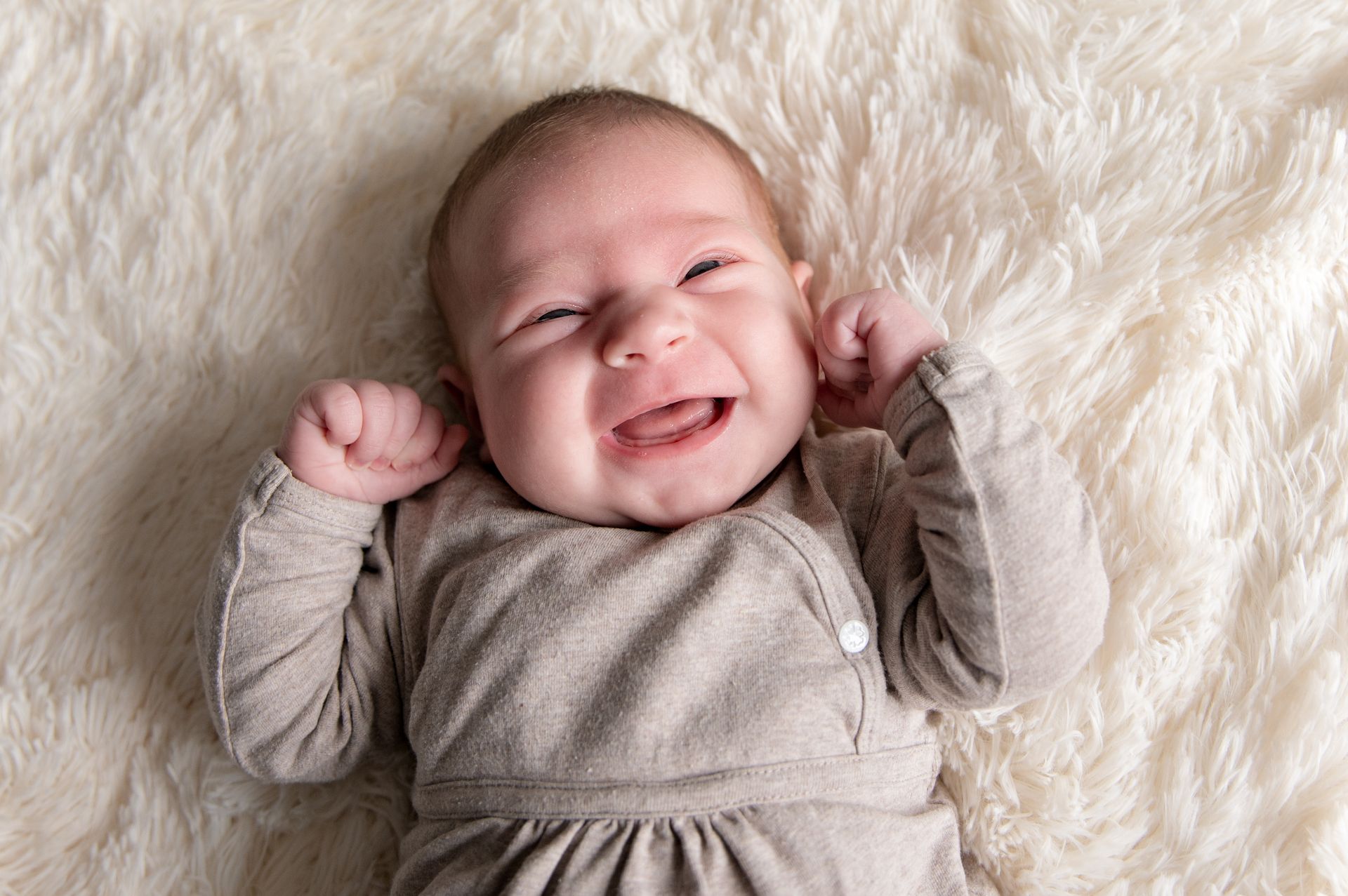 Een baby huilt terwijl hij op een deken op een bed ligt.