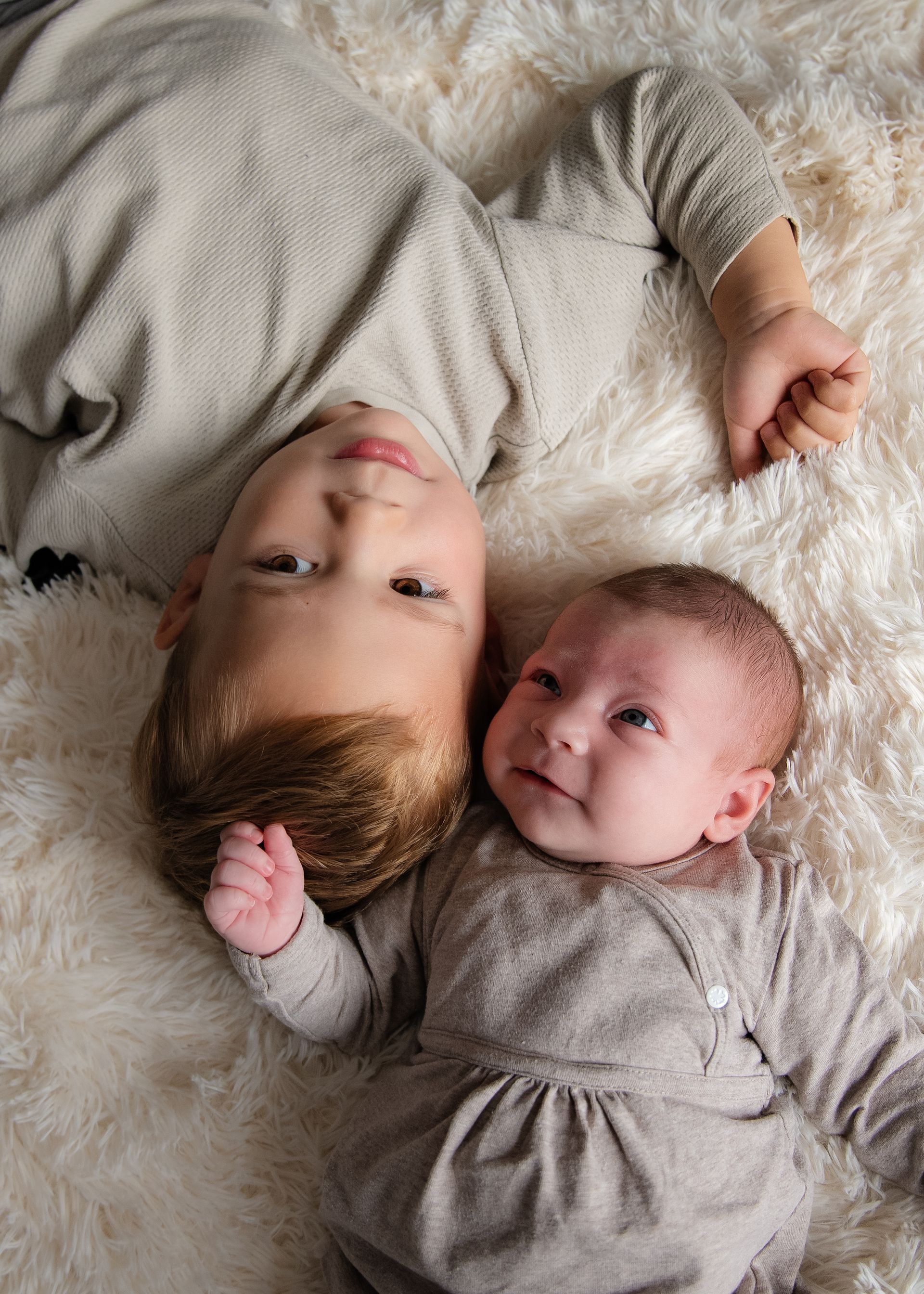 Een jongen en een baby liggen op een witte deken.