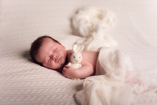 Een pasgeboren baby slaapt op een bed met een knuffelkonijn in zijn armen.